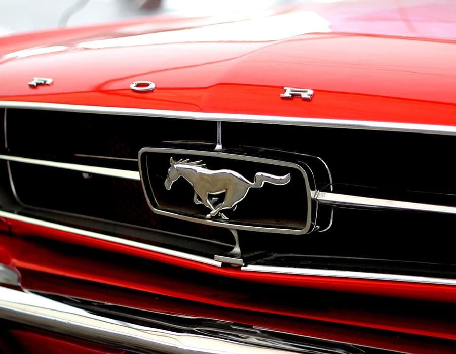 The front grille of a red Ford Mustang with its signature silver horse emblem centered on a black rectangular background.