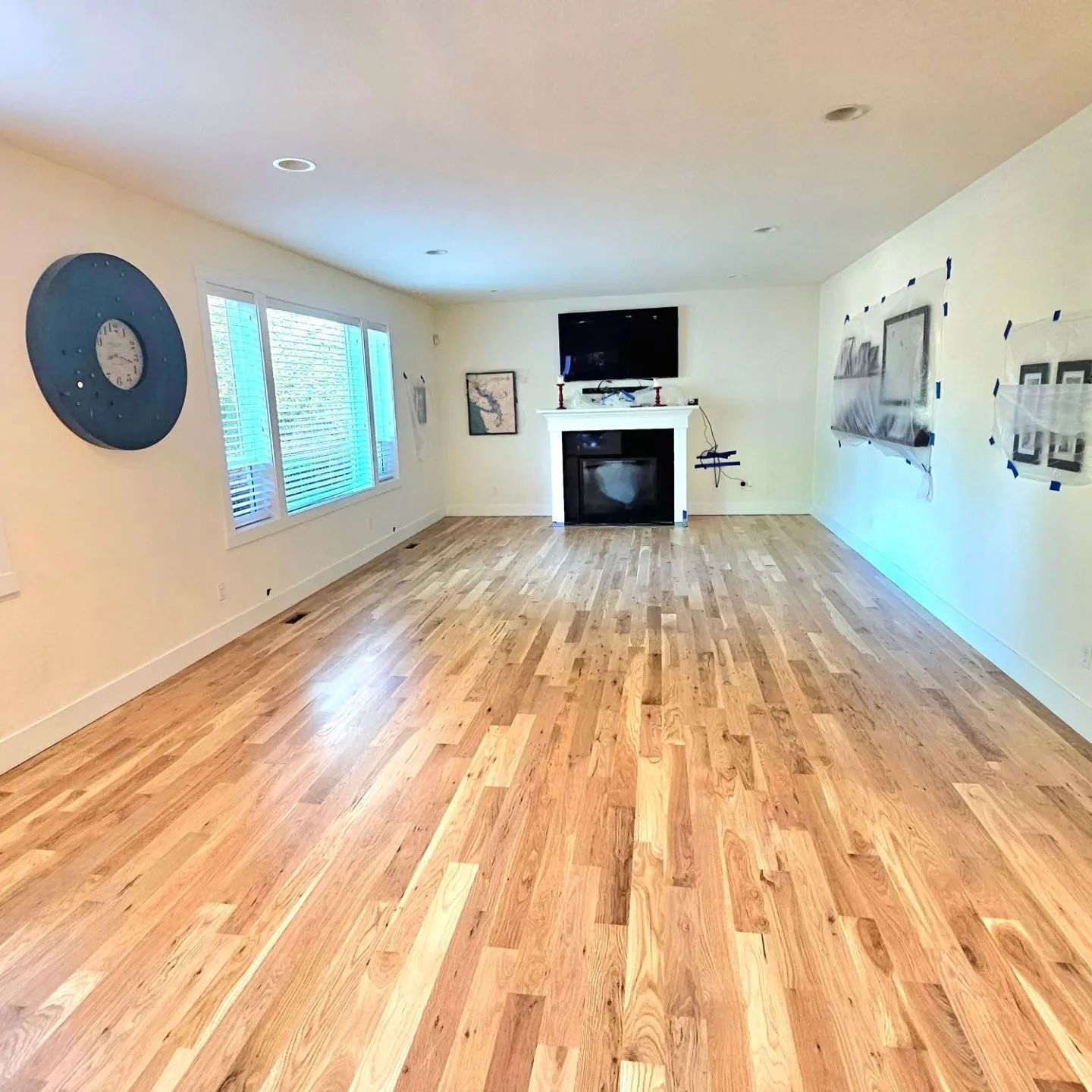 Empty living room with wood floor, fireplace, TV, and blue wall art.