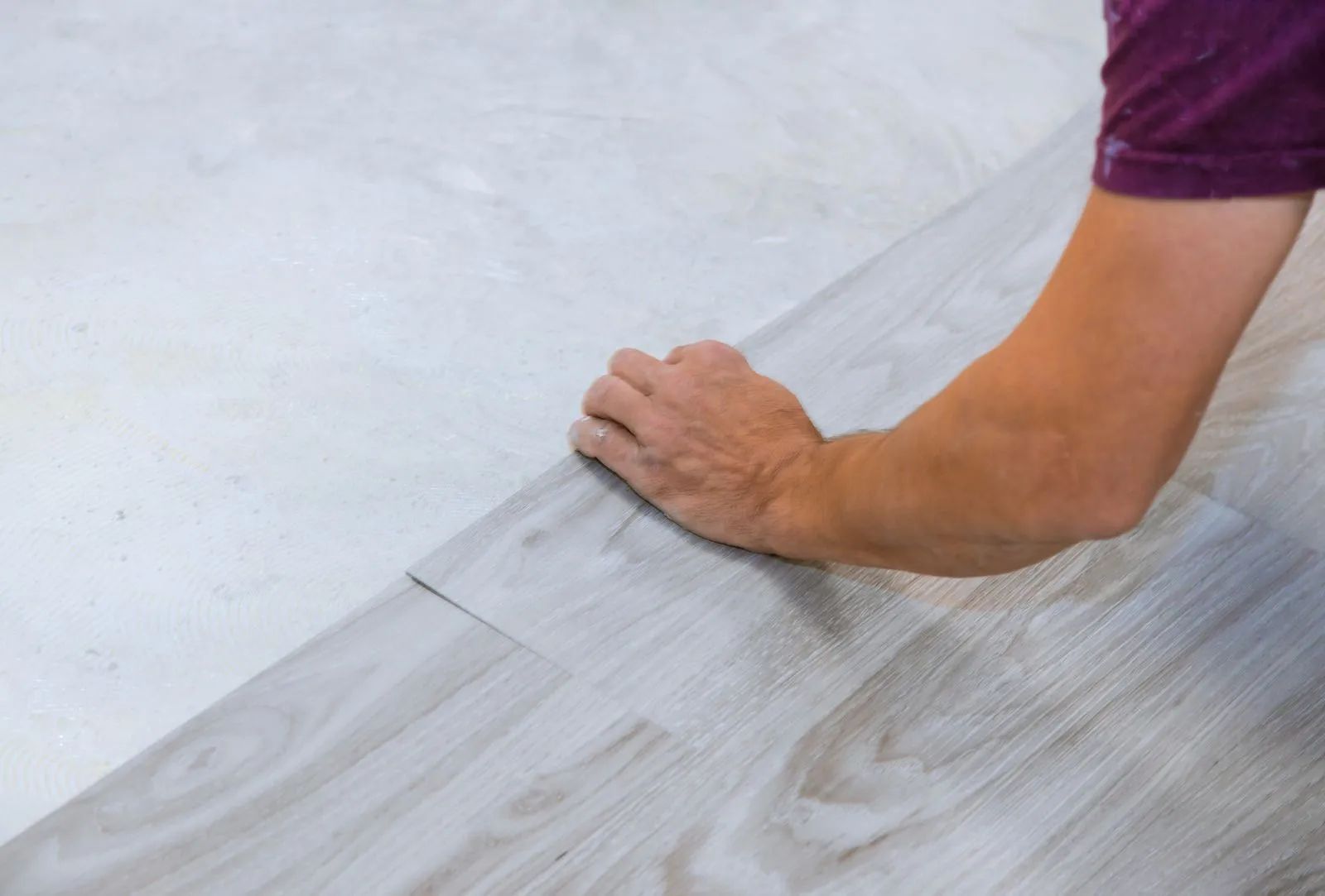 Person installing light wood-look flooring; hand placing a plank on the floor next to existing
plank