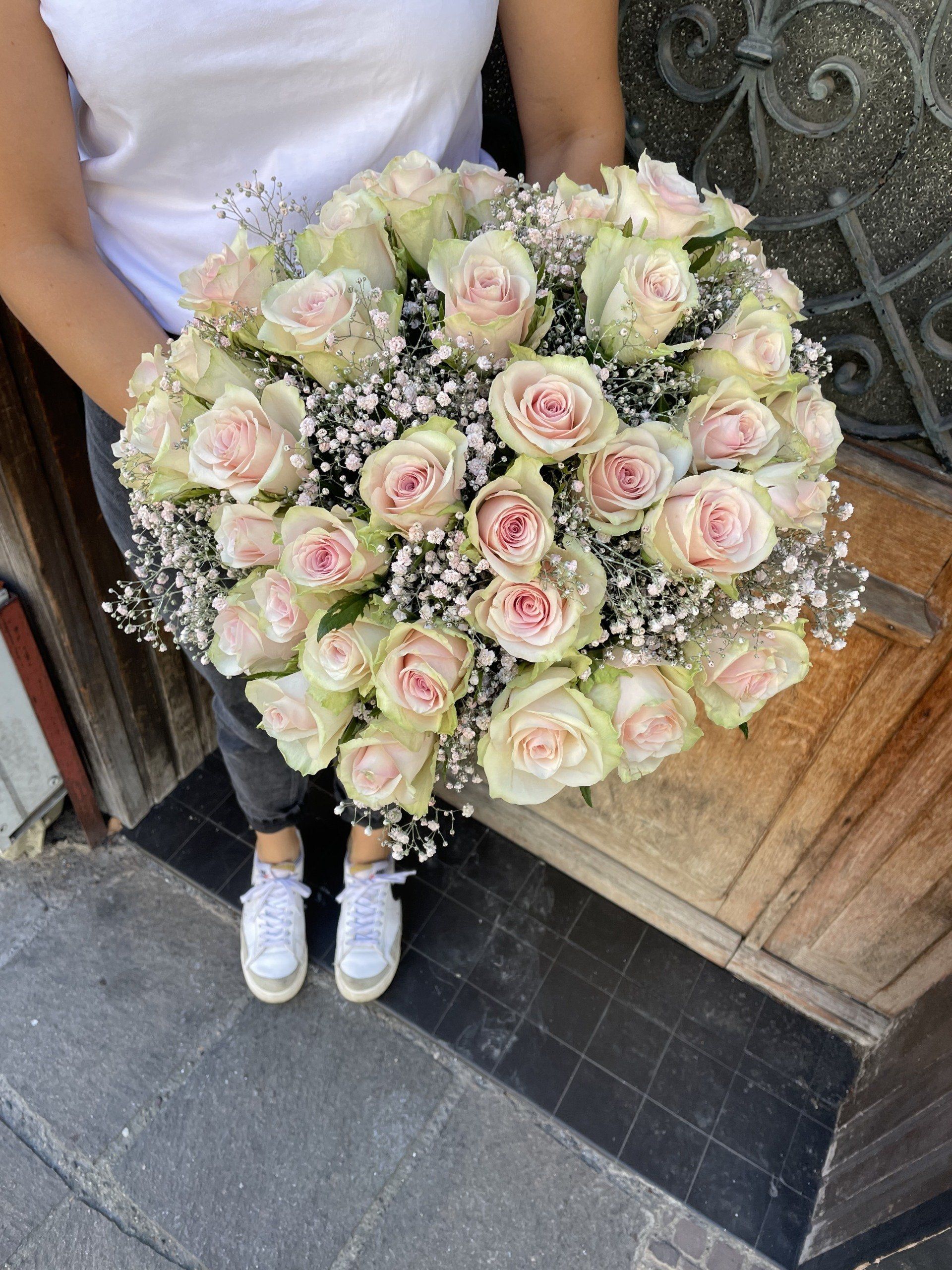 Une femme tient un grand bouquet de roses roses et de gypsophile.