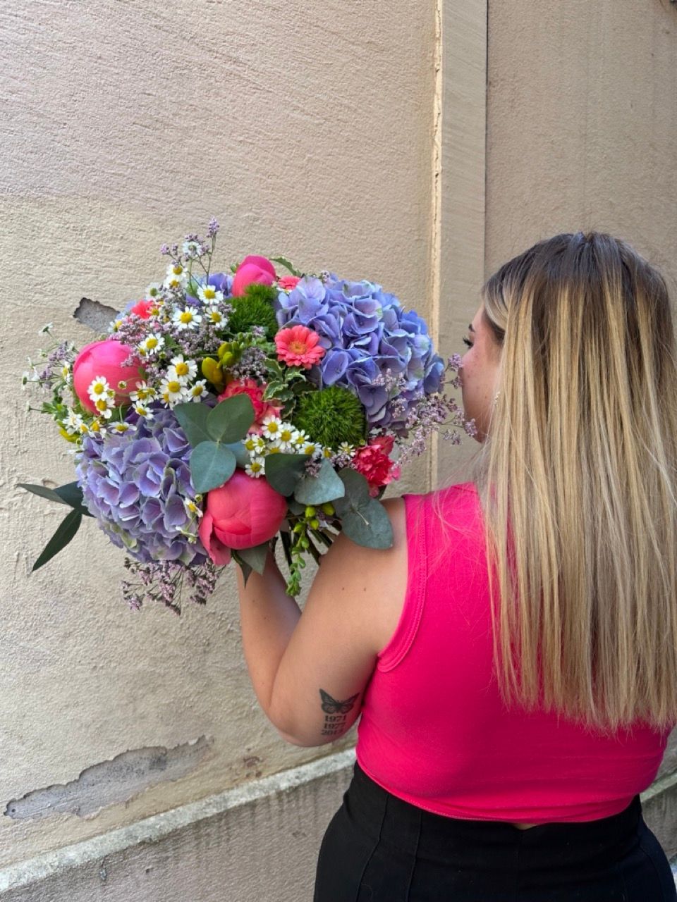 Une femme en débardeur rose tient un gros bouquet de fleurs.