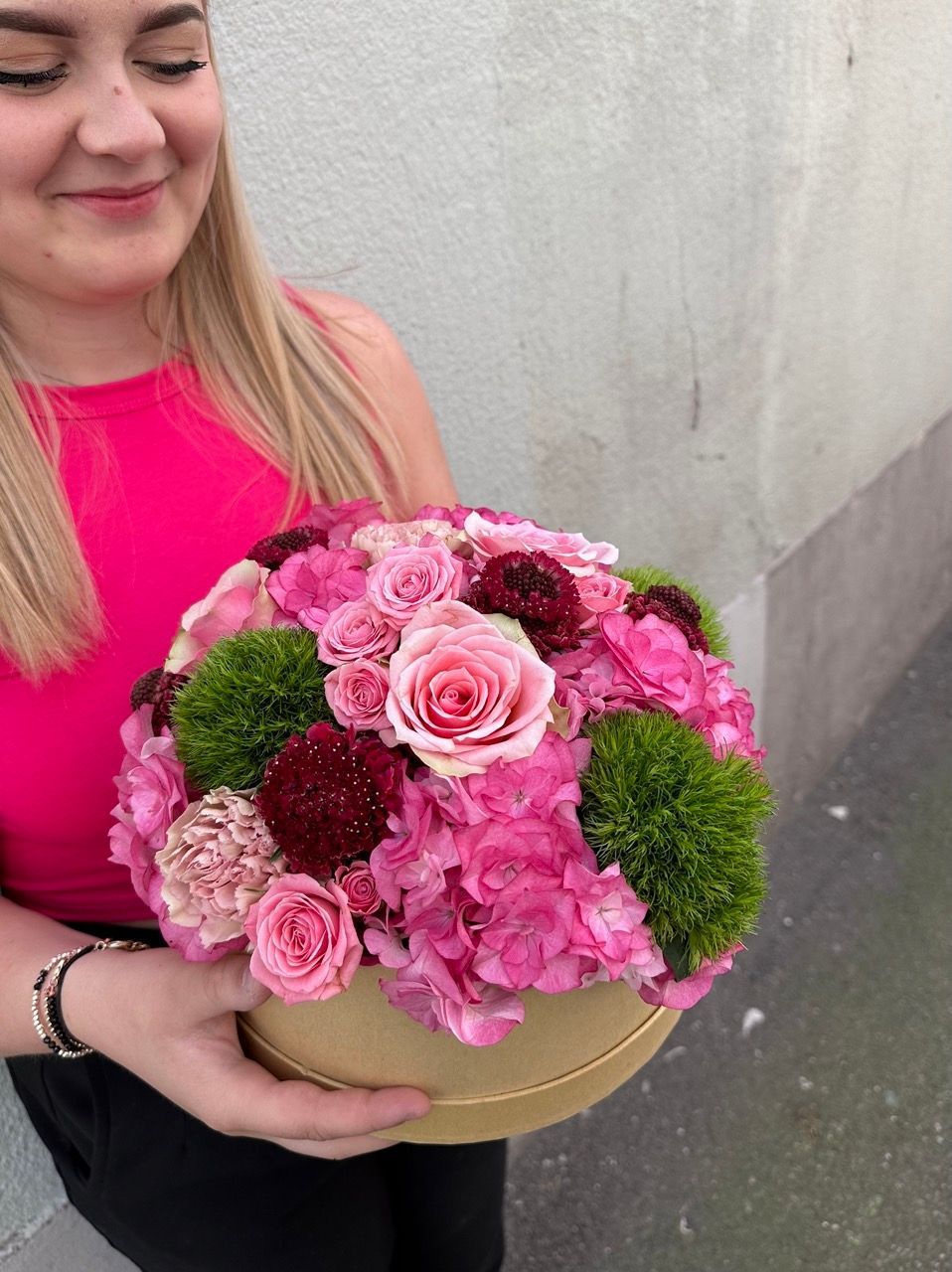 Une femme tient une boîte ronde remplie de fleurs roses.