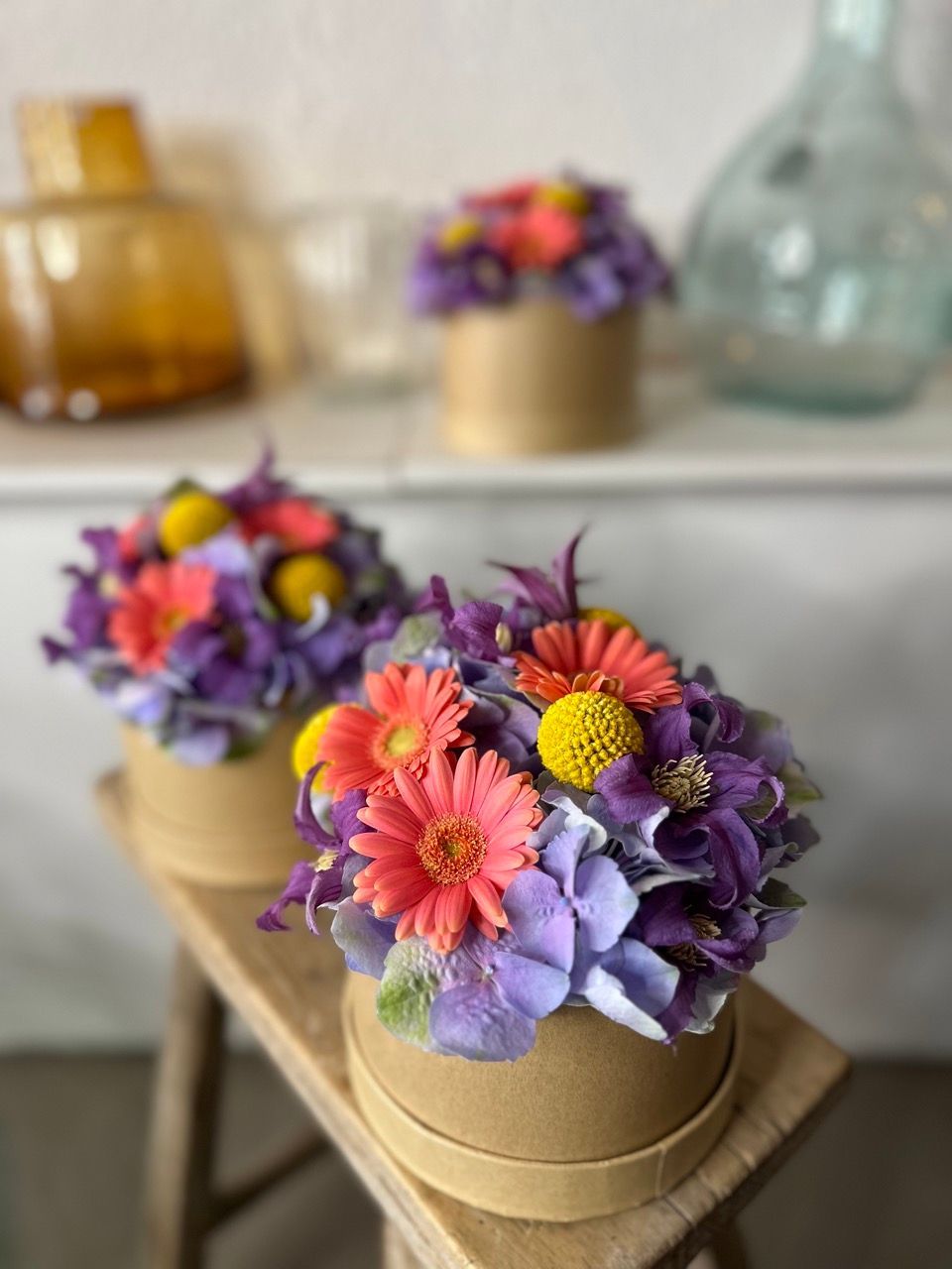 Trois boîtes remplies de fleurs sont posées sur un tabouret en bois.