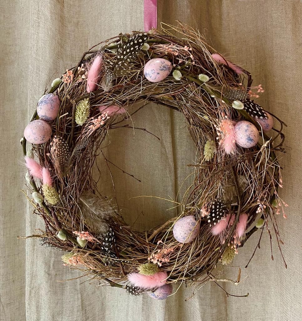 Une couronne avec des œufs et des fleurs roses est accrochée au mur.