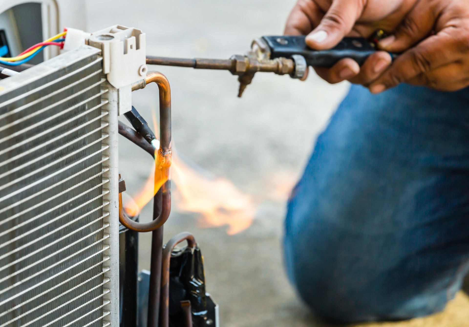 Person using a torch to solder copper tubing on an air conditioning unit.