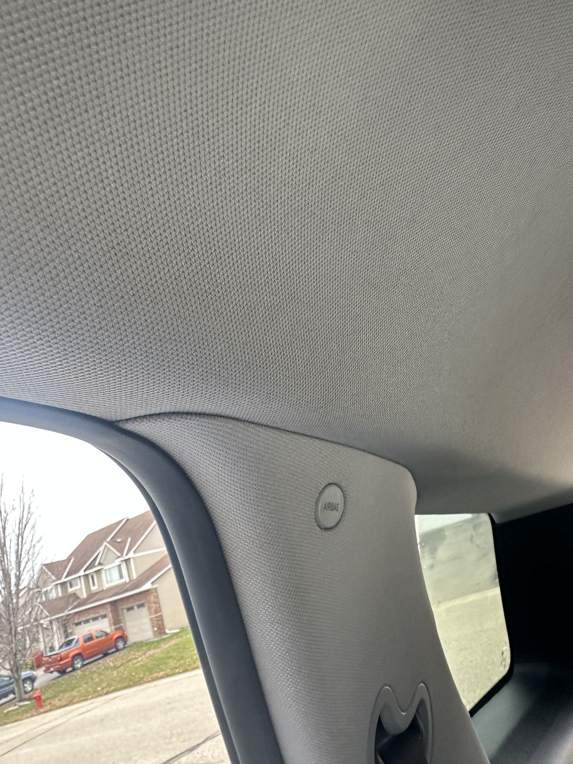 Interior view of a gray car's roof lining and pillar, showing an airbag warning symbol on the pillar near a window.