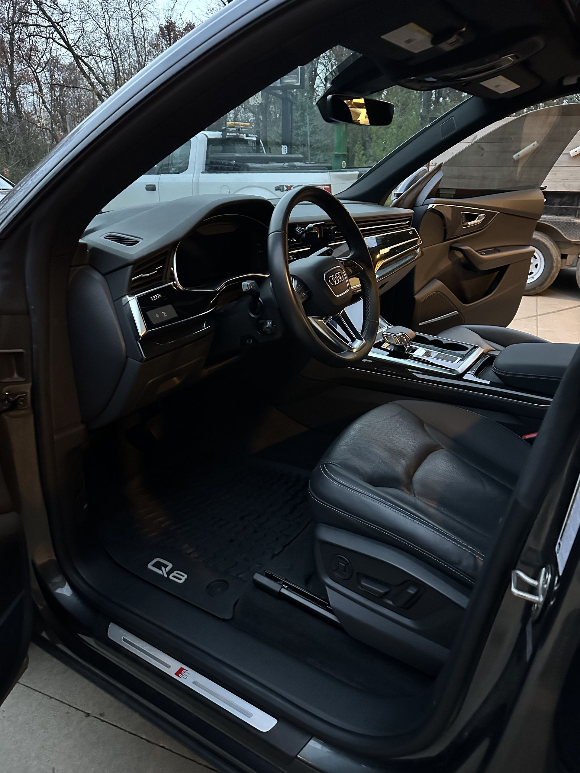 Driver’s side interior of a dark gray Audi Q5, showing the leather bucket seat, steering wheel, and dashboard.
