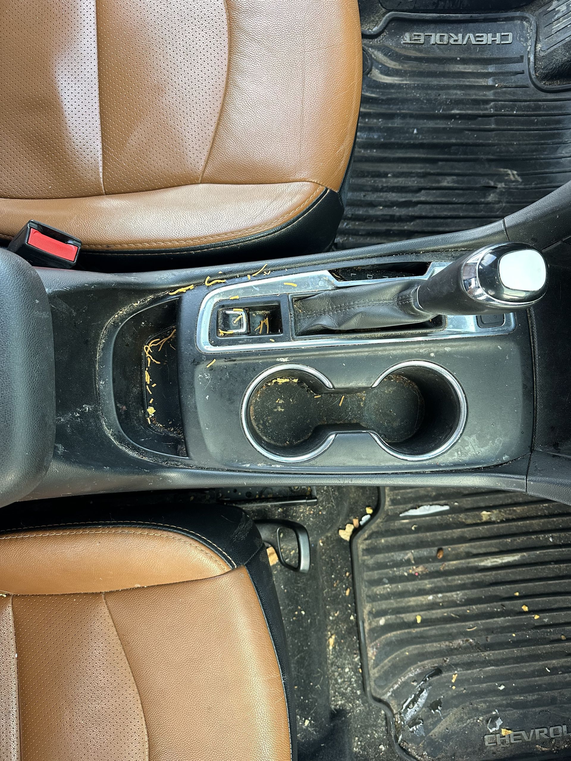 A car interior showing a dusty center console with two cup holders, a gear shifter, and tan and black leather seats.