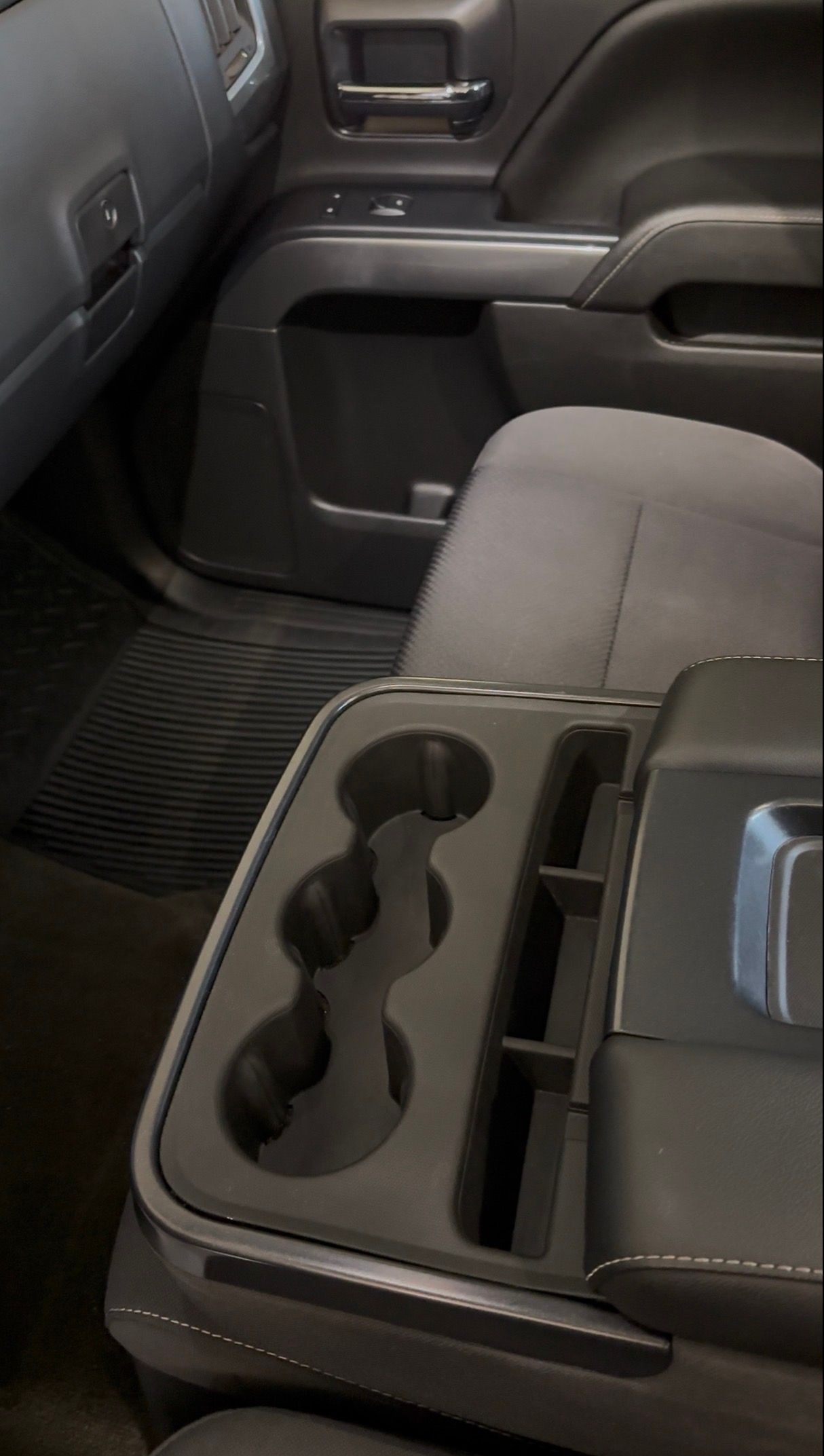 A car interior view of a center console featuring three molded cup holders and a storage slot next to a gray cloth seat.