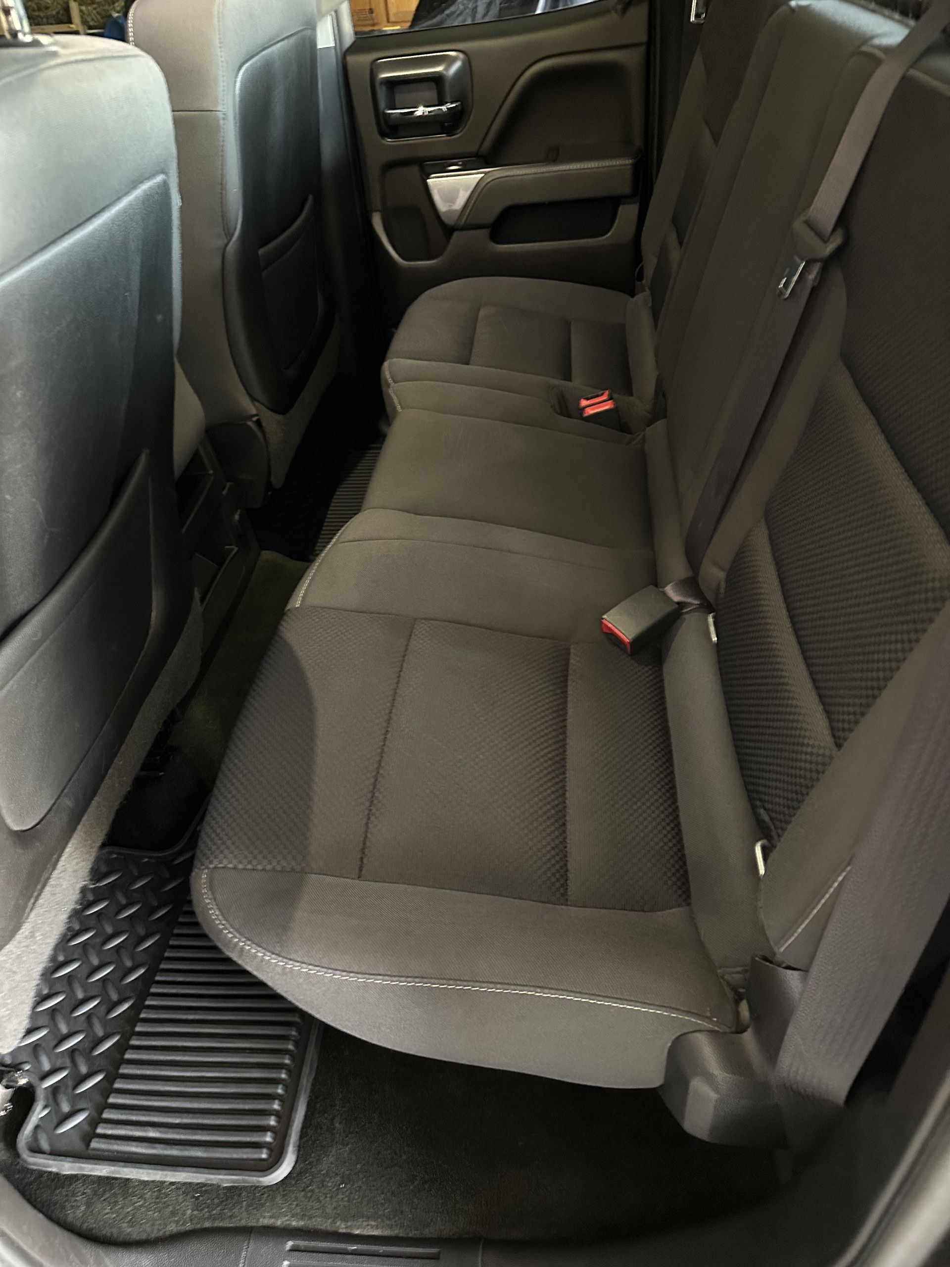 The interior back seat of a truck, featuring dark gray cloth upholstery and black rubber floor mats.