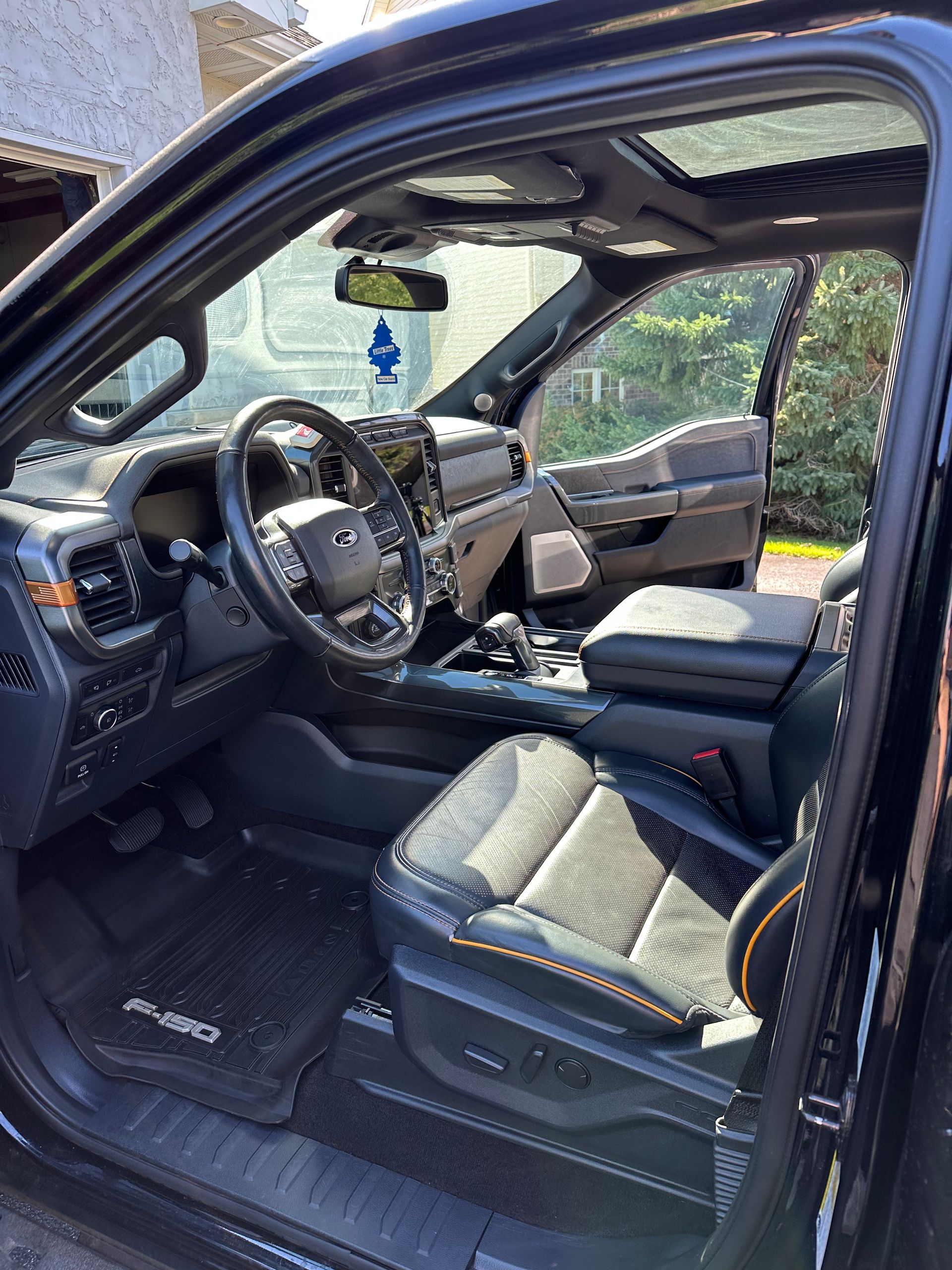 The interior of a modern black truck featuring dark leather seats with orange stitching, a sunroof, and a steering wheel.