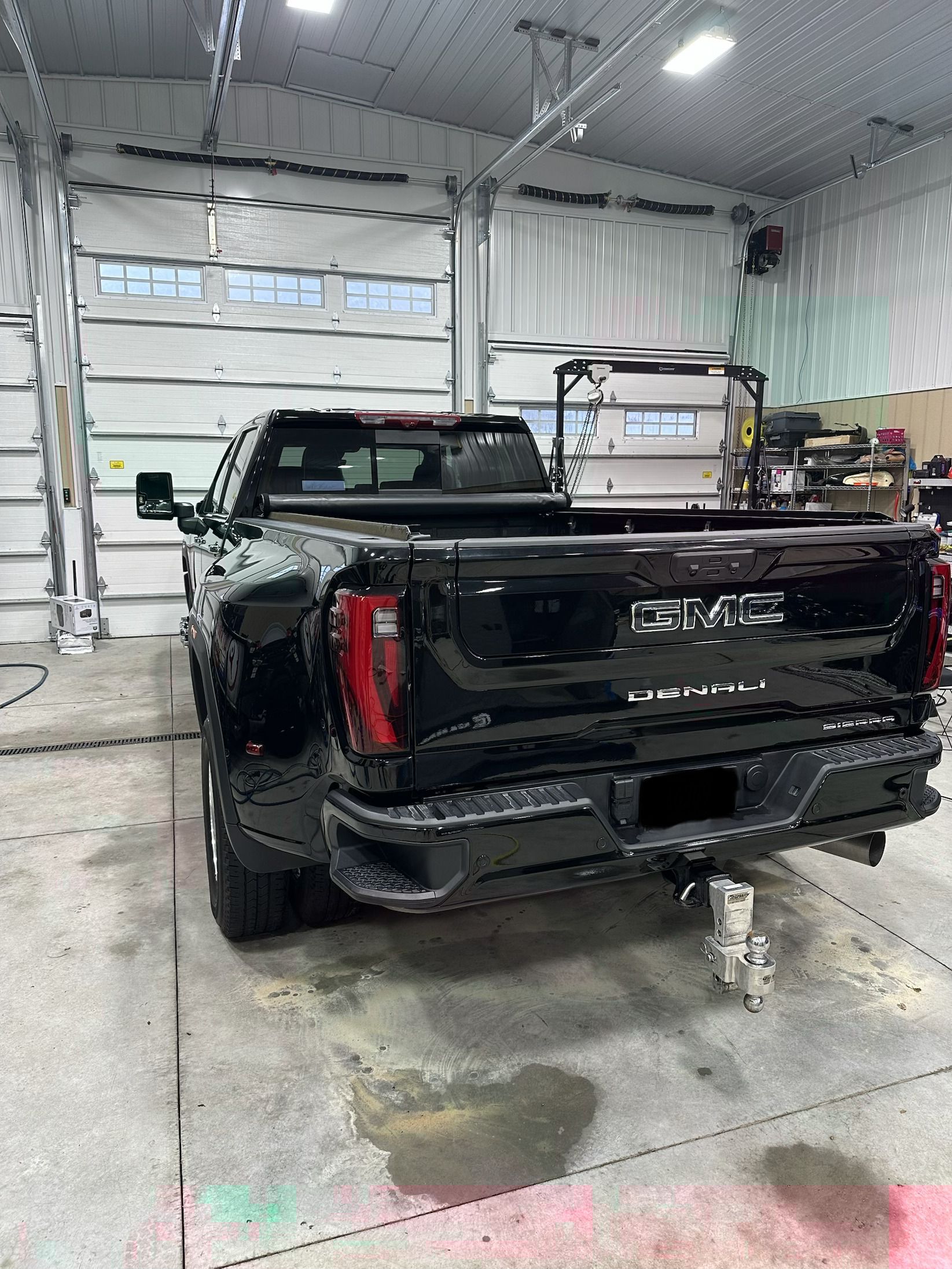 A black GMC pickup truck parked inside a bright, industrial garage with a white roll-up door.