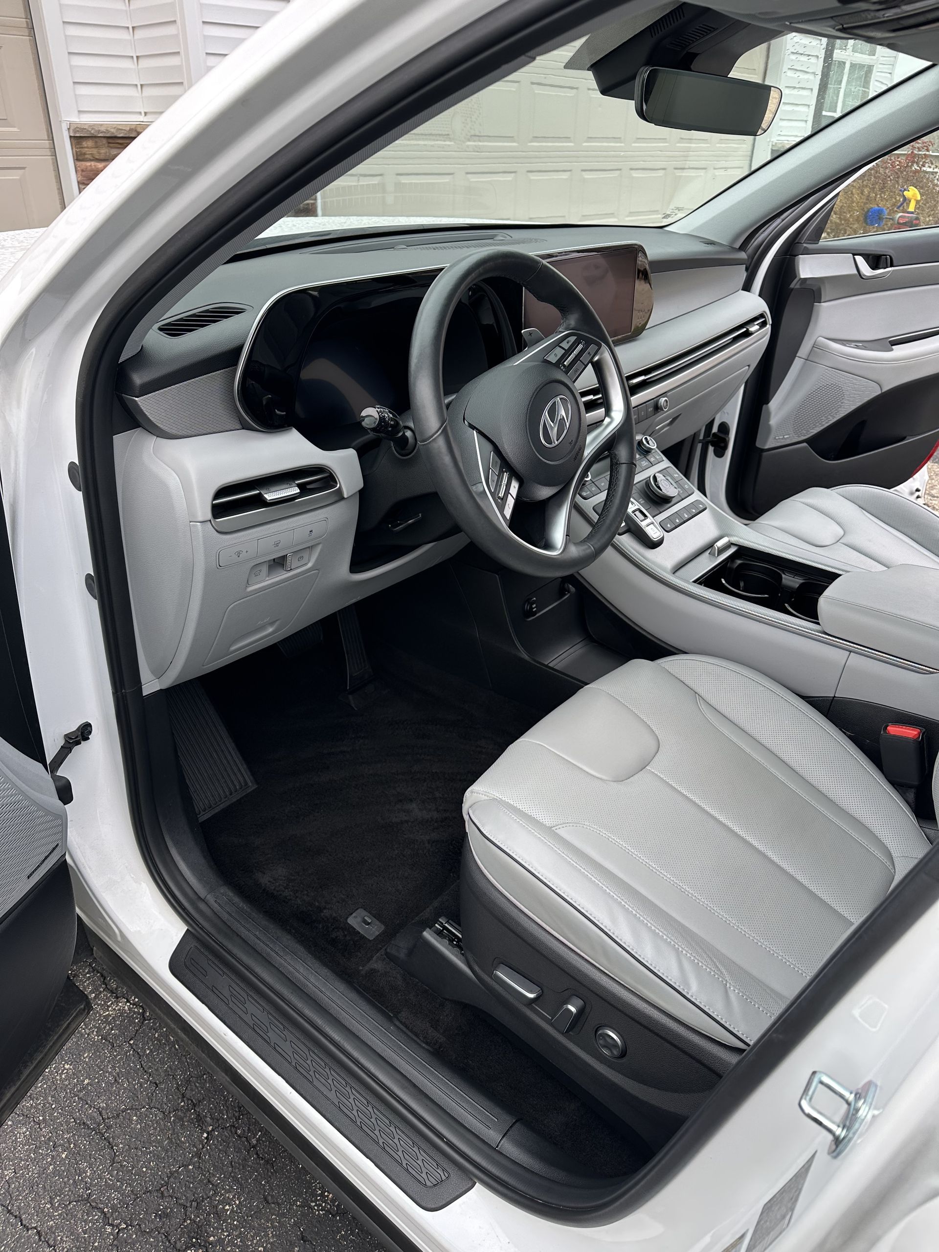 Interior of a modern white SUV showing a gray leather driver seat, dashboard controls, and a multi-function steering wheel.