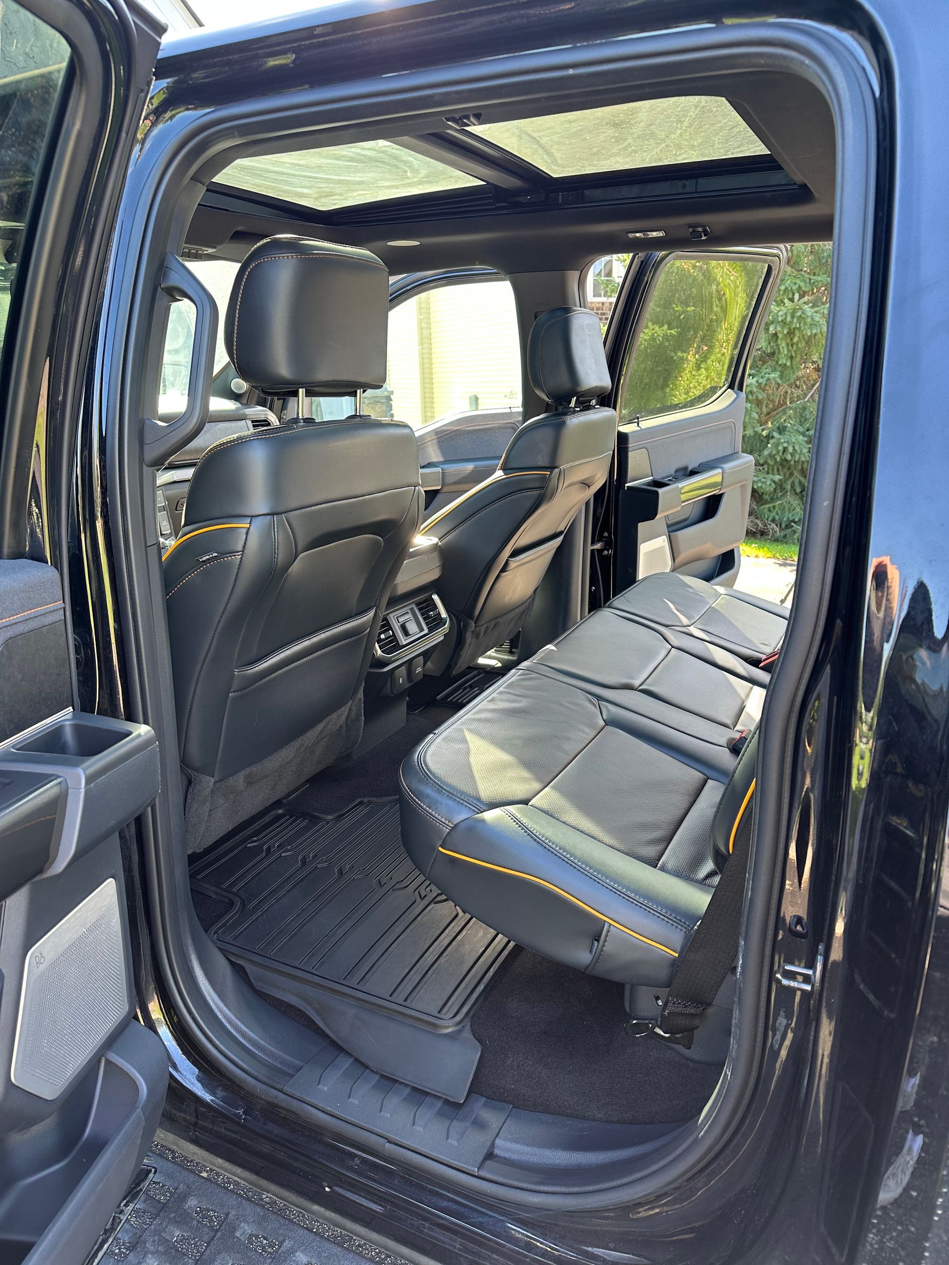 The interior of a black pickup truck with dark leather seats, yellow stitching, and a panoramic sunroof.