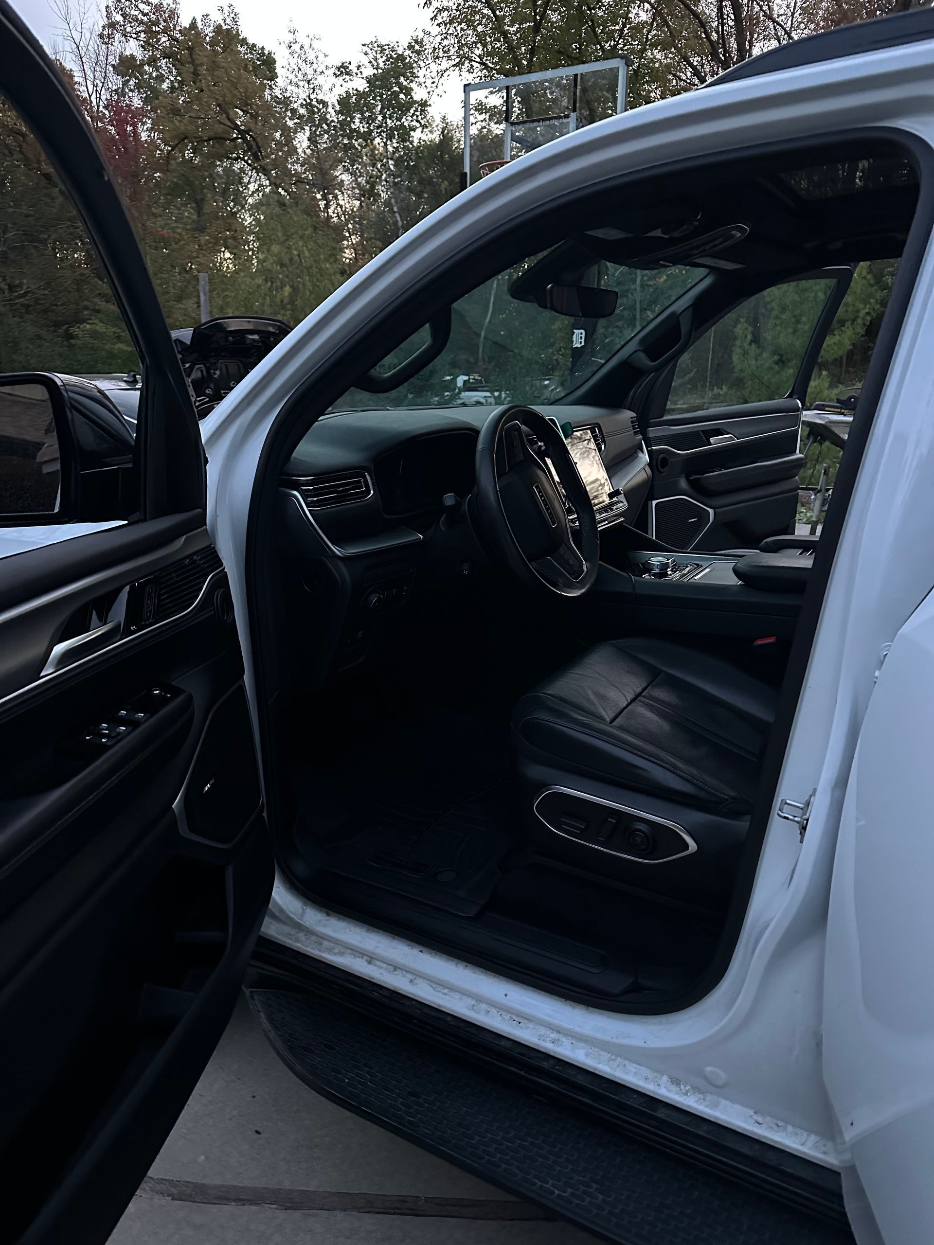 The open driver-side door of a white SUV reveals a black leather interior, steering wheel, and dashboard.
