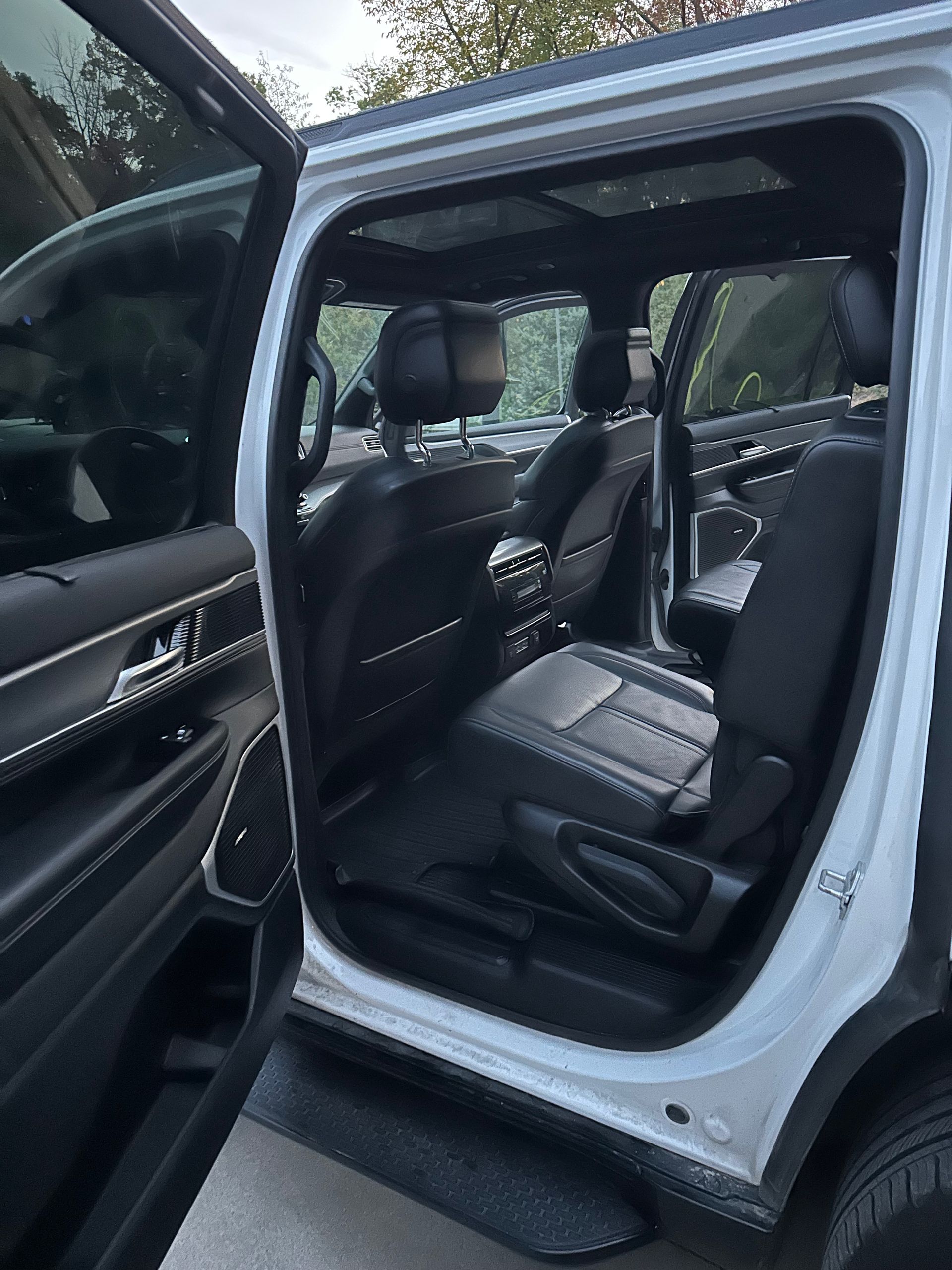 A view from the open rear door of a white SUV, showing black leather seats and a panoramic sunroof.