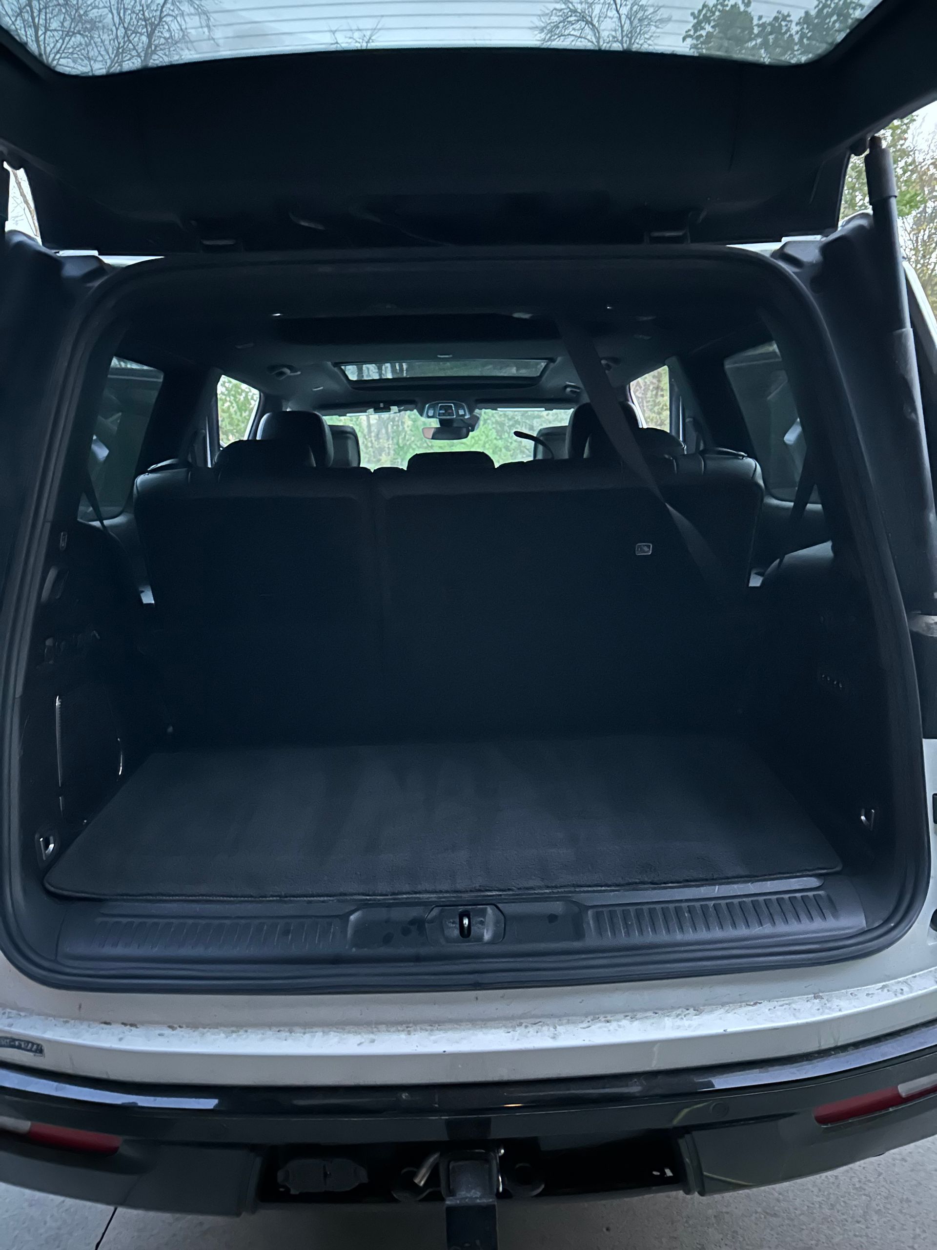 The open cargo area of a silver SUV showing a dark interior with a mat on the floor and the rear seats upright.