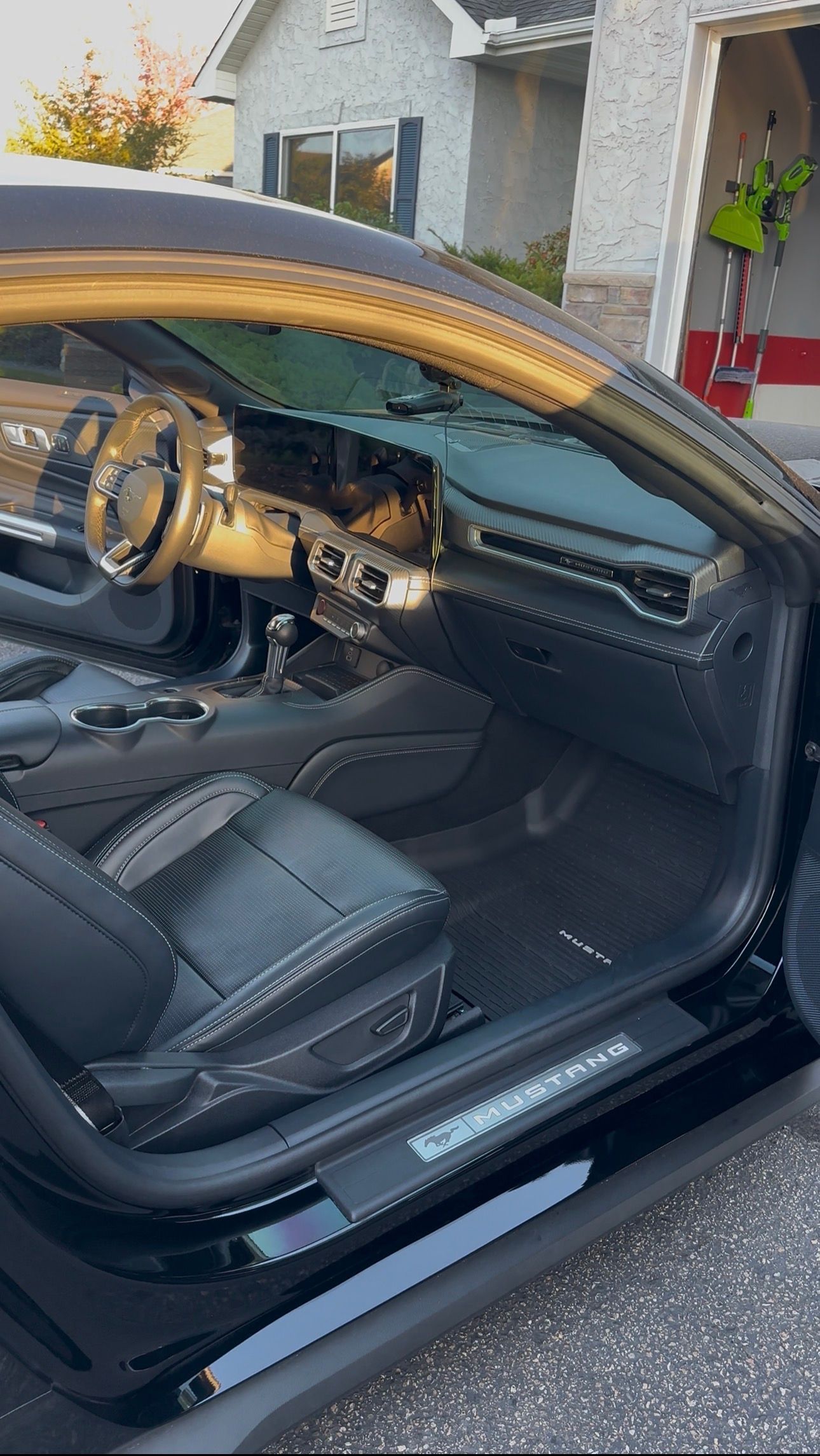 A close-up of a car's black interior, featuring textured leather seats and gold-colored trim accents, parked in a driveway.
