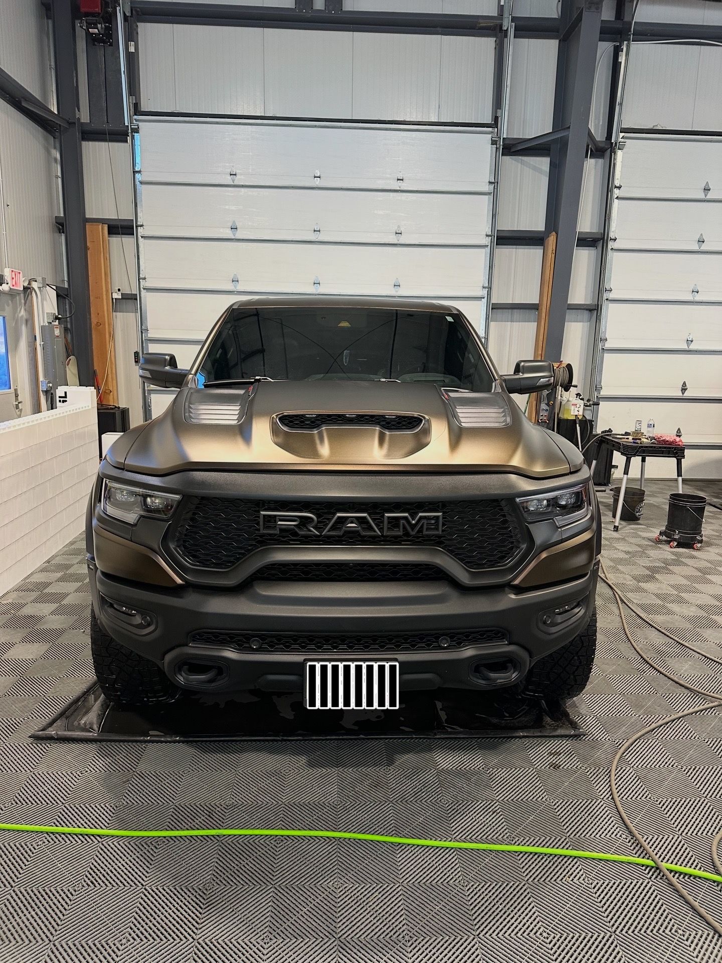 A matte bronze and black Ram TRX pickup truck parked inside a bright, industrial garage with a patterned floor.