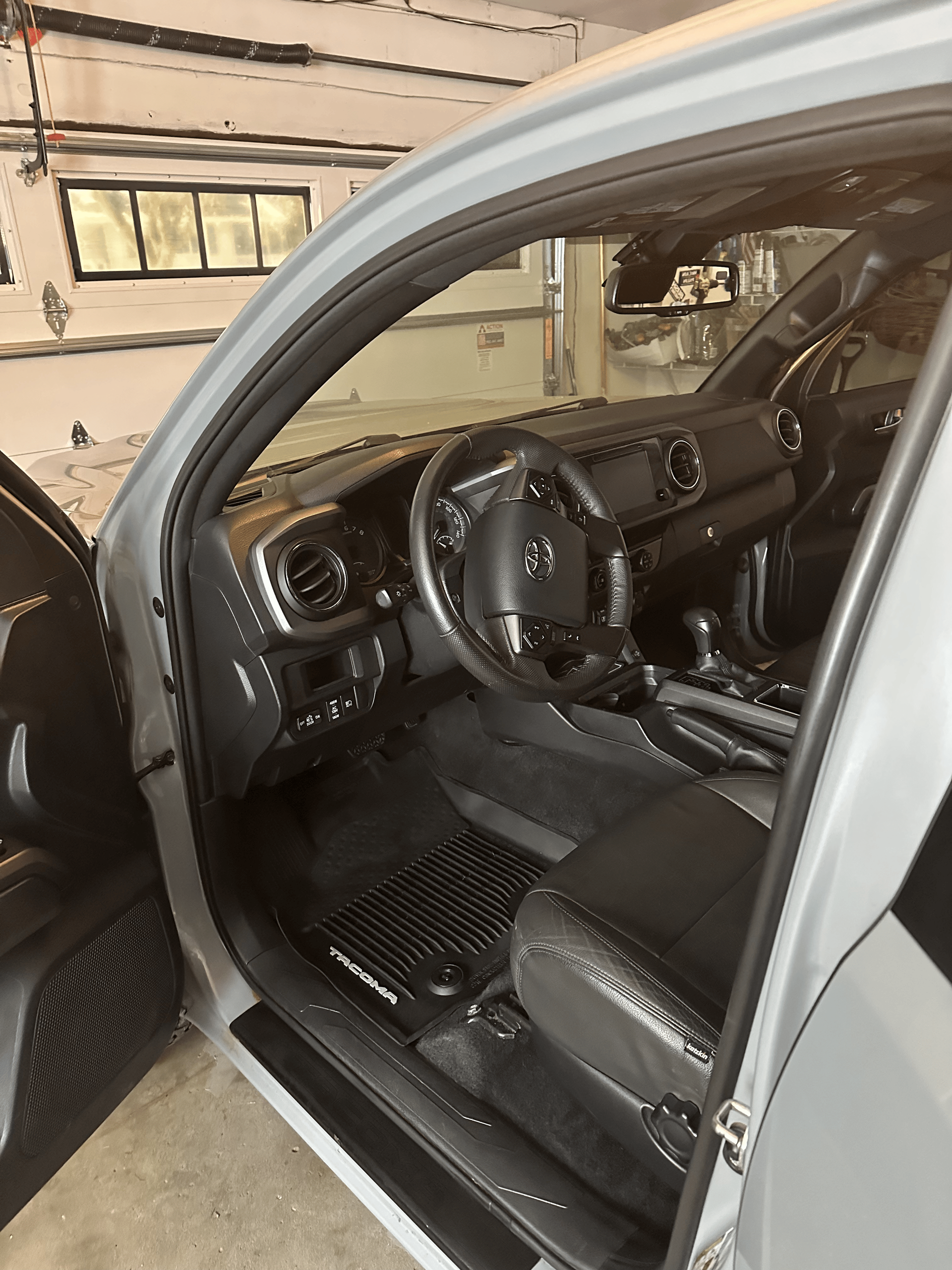 Interior of a gray vehicle, showing the driver's seat, steering wheel, dashboard, and black floor mats.