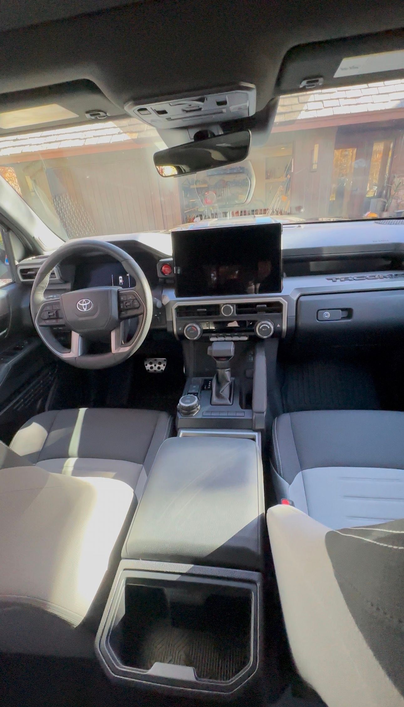 The interior view of a vehicle, showing a steering wheel, center dashboard touchscreen, and gray cloth front seats.