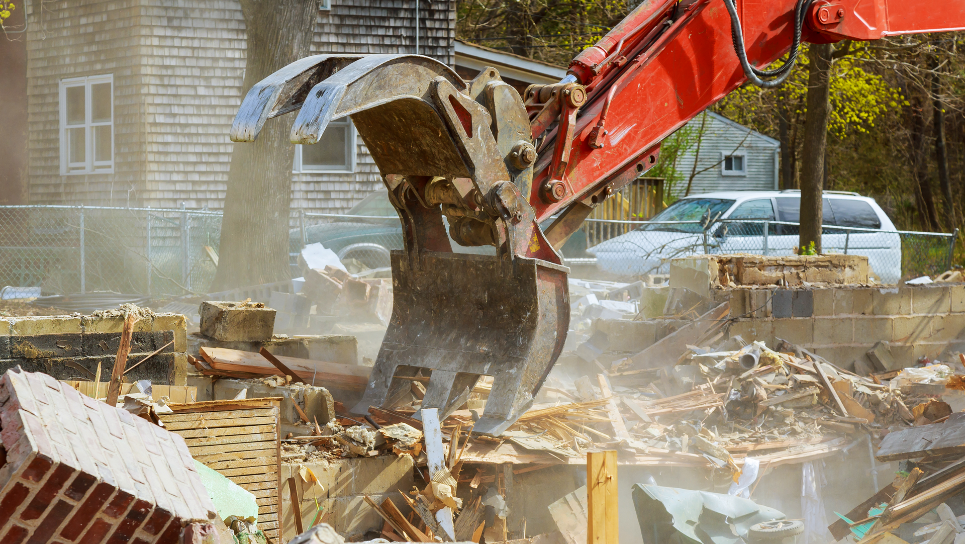 A large red excavator is demolishing a house.