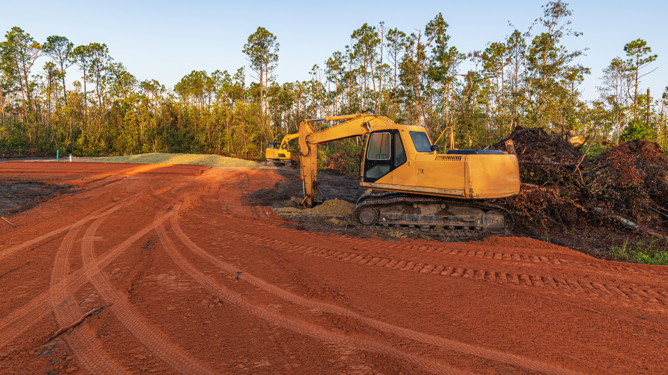 A yellow excavator is working on a dirt road.