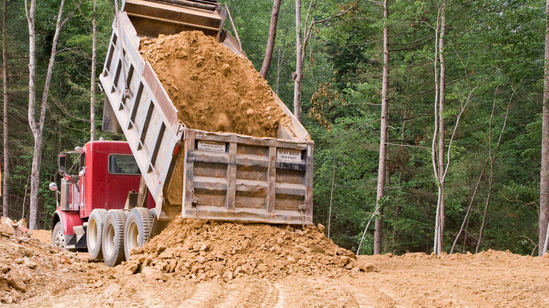 A dump truck is dumping dirt into a pile.