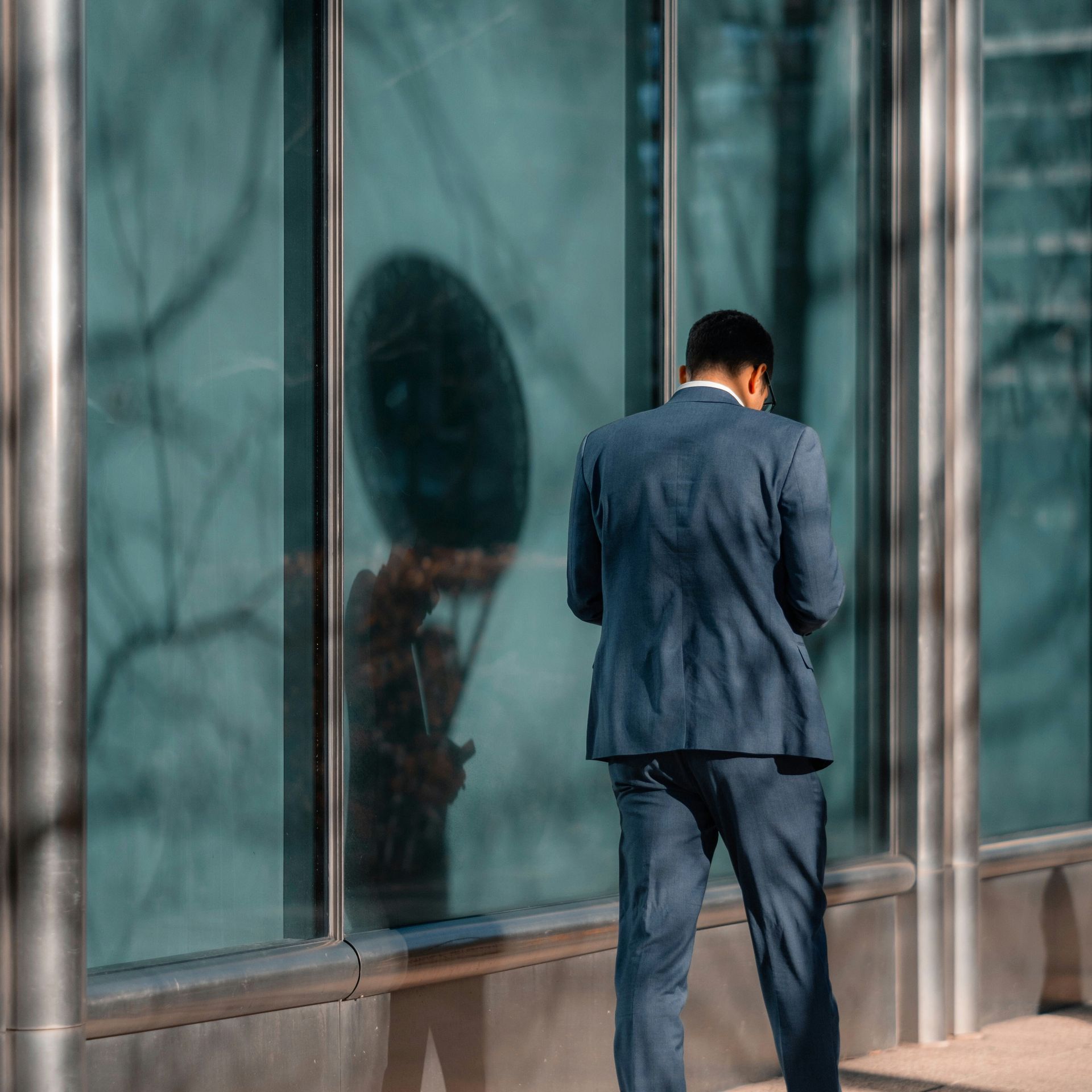 A man in a suit is standing in front of a building looking at his phone.