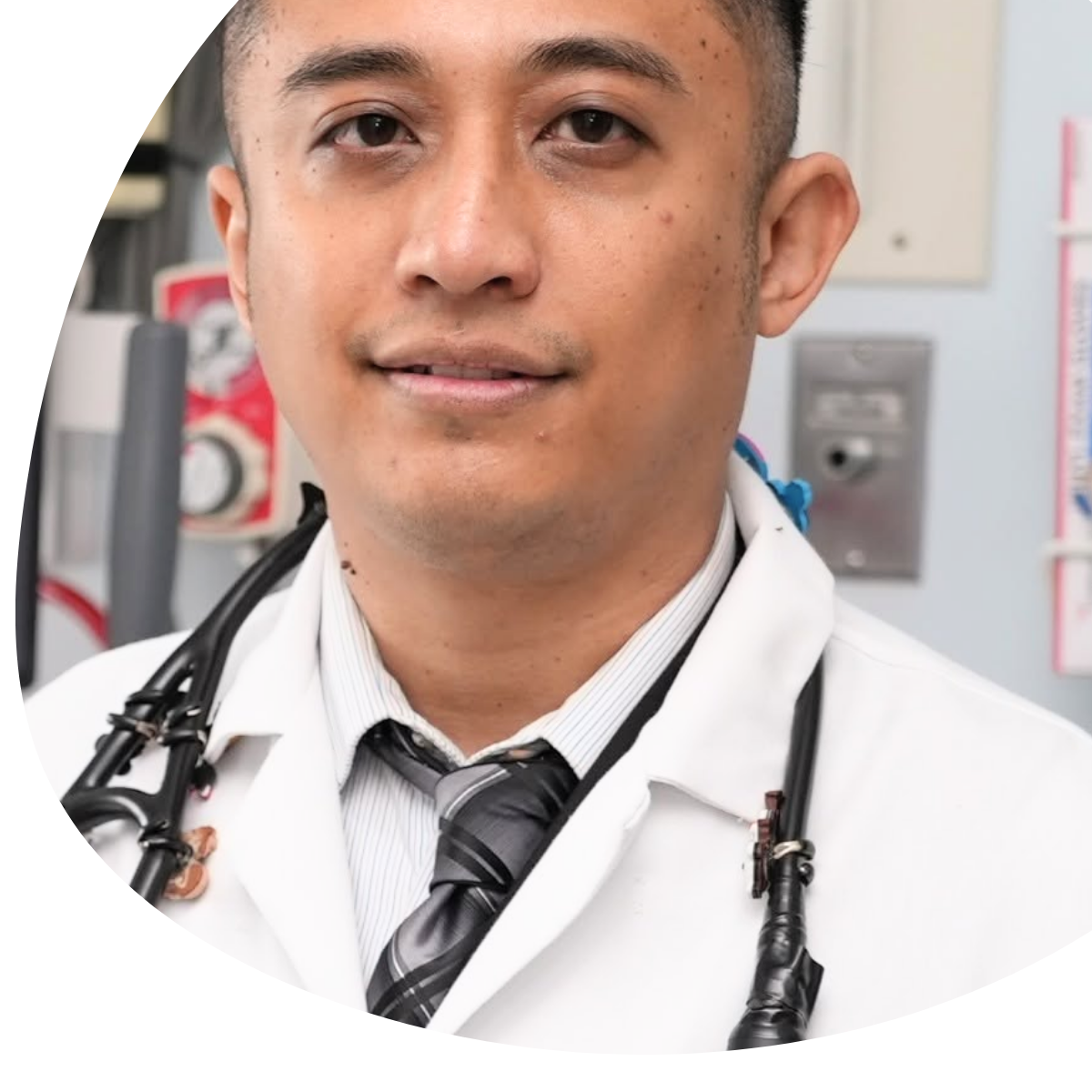 Smiling doctor in a white coat with a stethoscope, standing with arms crossed in a bright clinic hallway