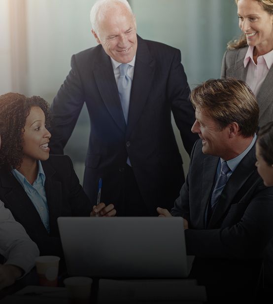 Business team in suits at a table with laptop, discussing. Smiling, professional setting.
