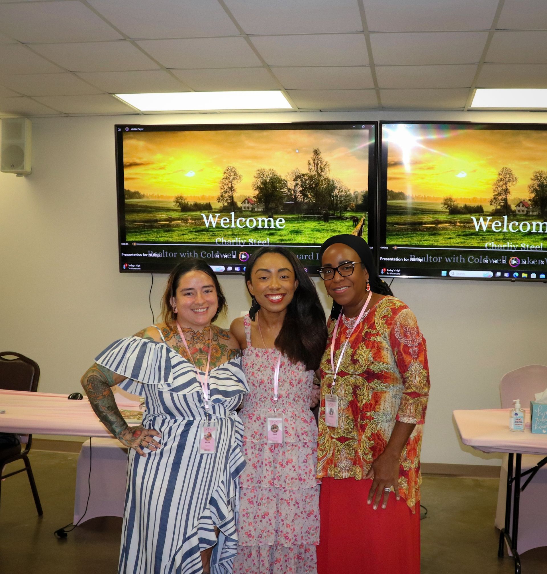 Three women are posing for a picture in front of a screen that says welcome