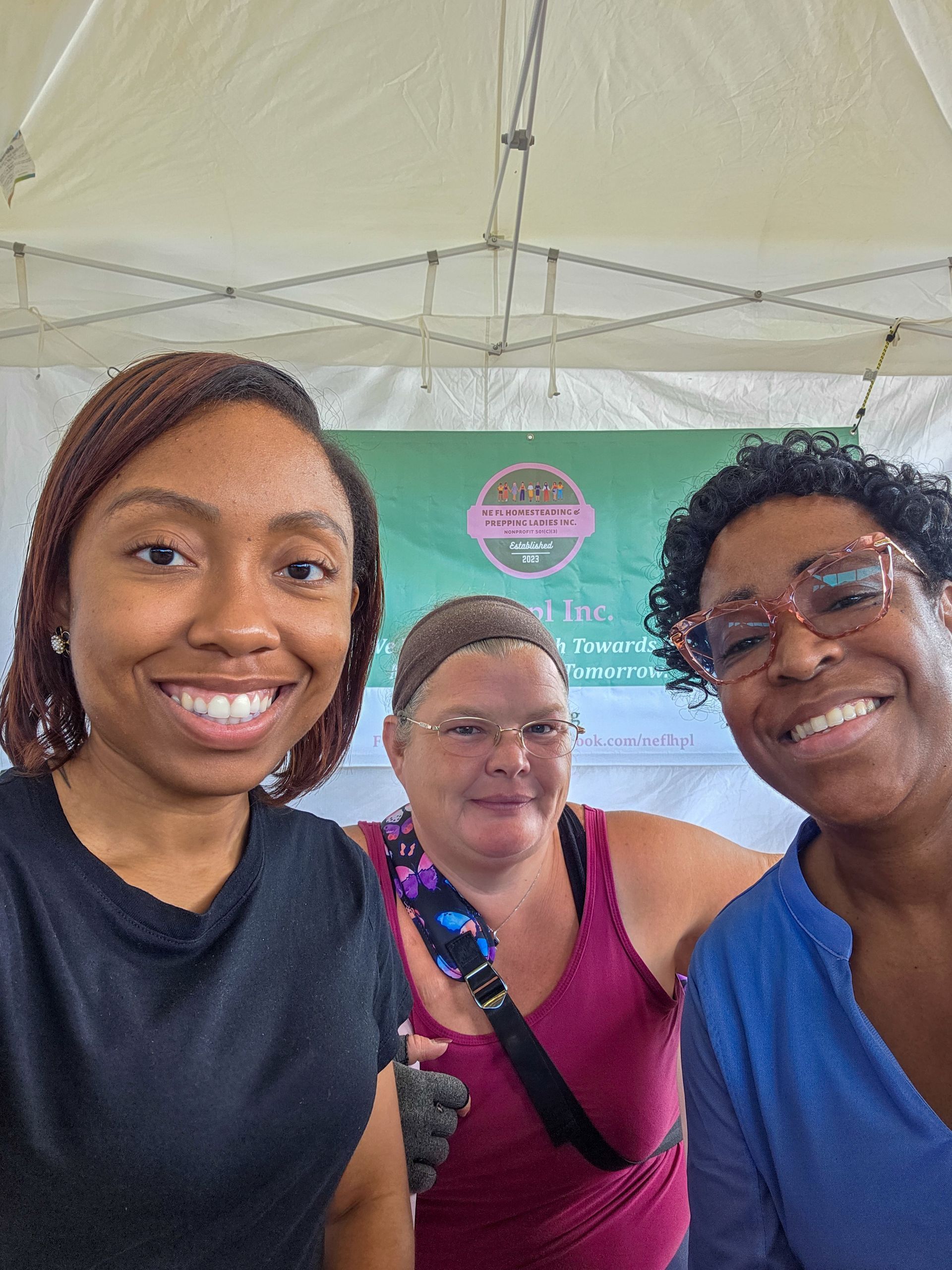 Three women are posing for a selfie in front of a tent.
