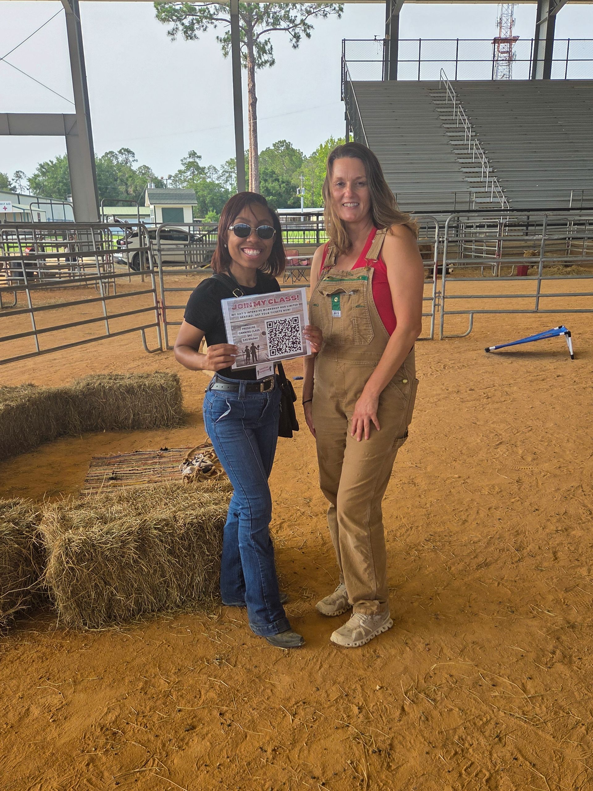 Two women are standing next to each other in a dirt field holding a piece of paper.