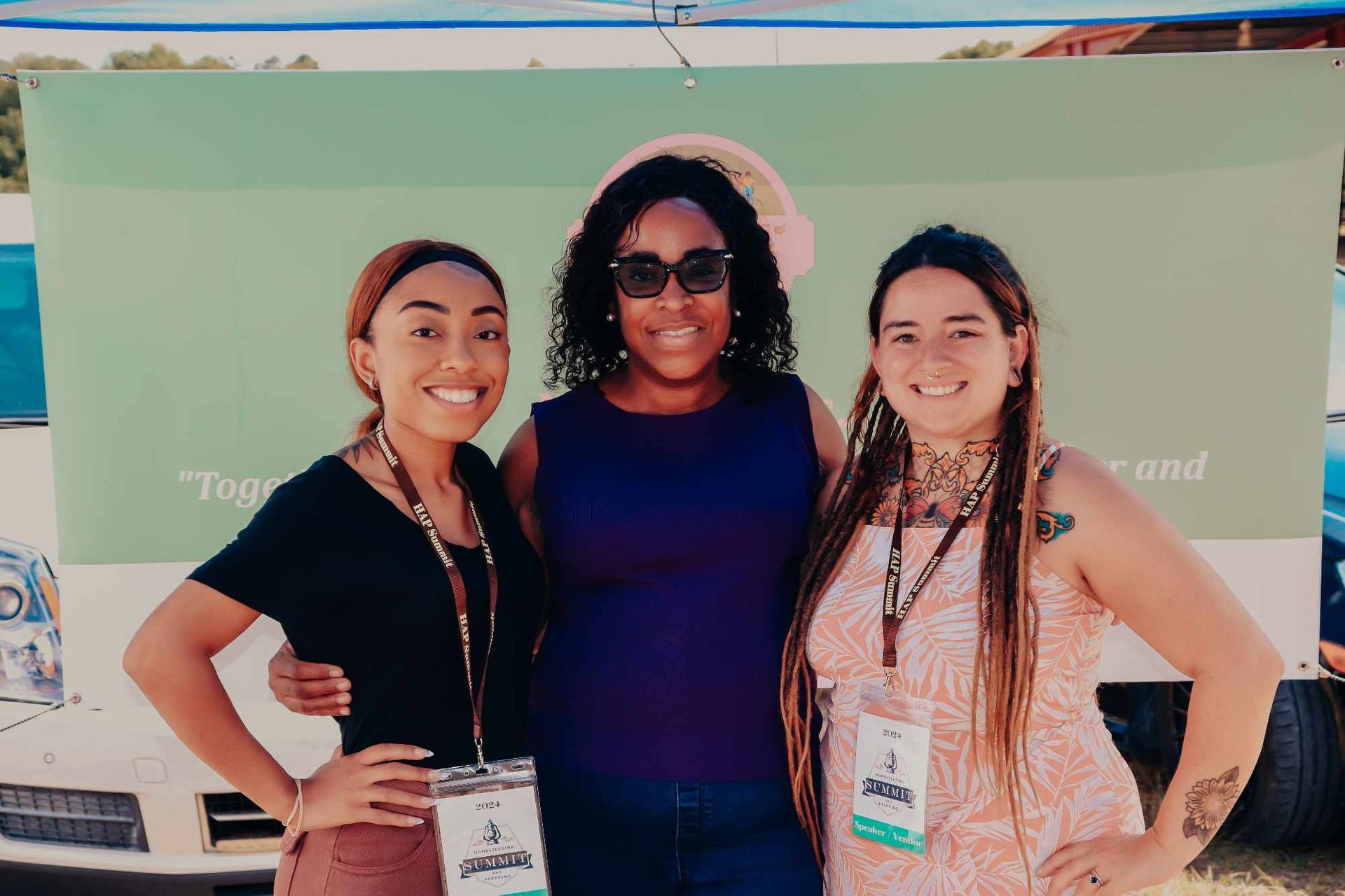 Three women are posing for a picture in front of a truck.