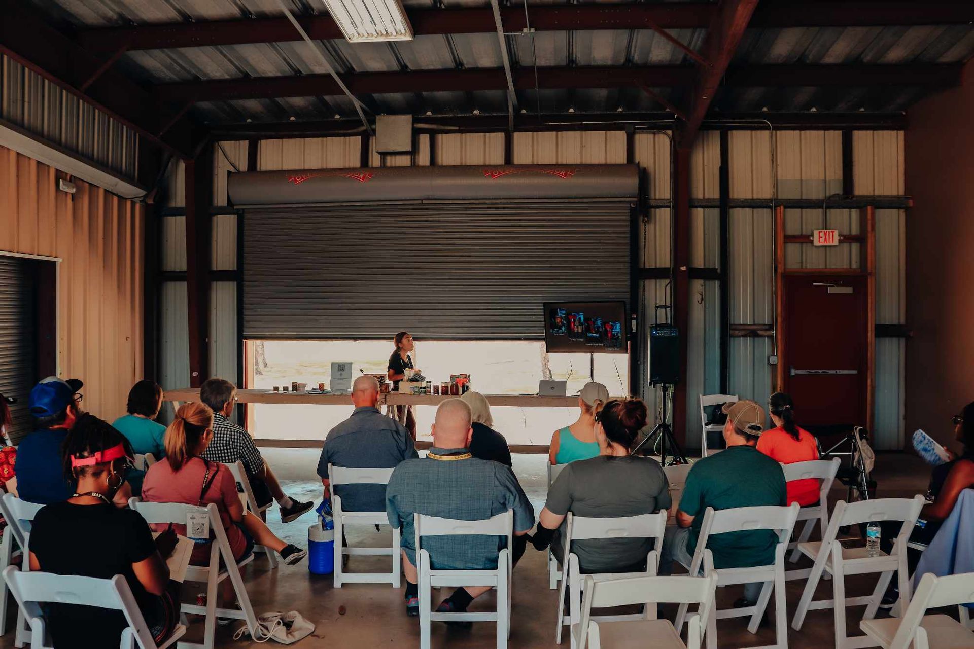 A group of people are sitting in white folding chairs in front of a stage.