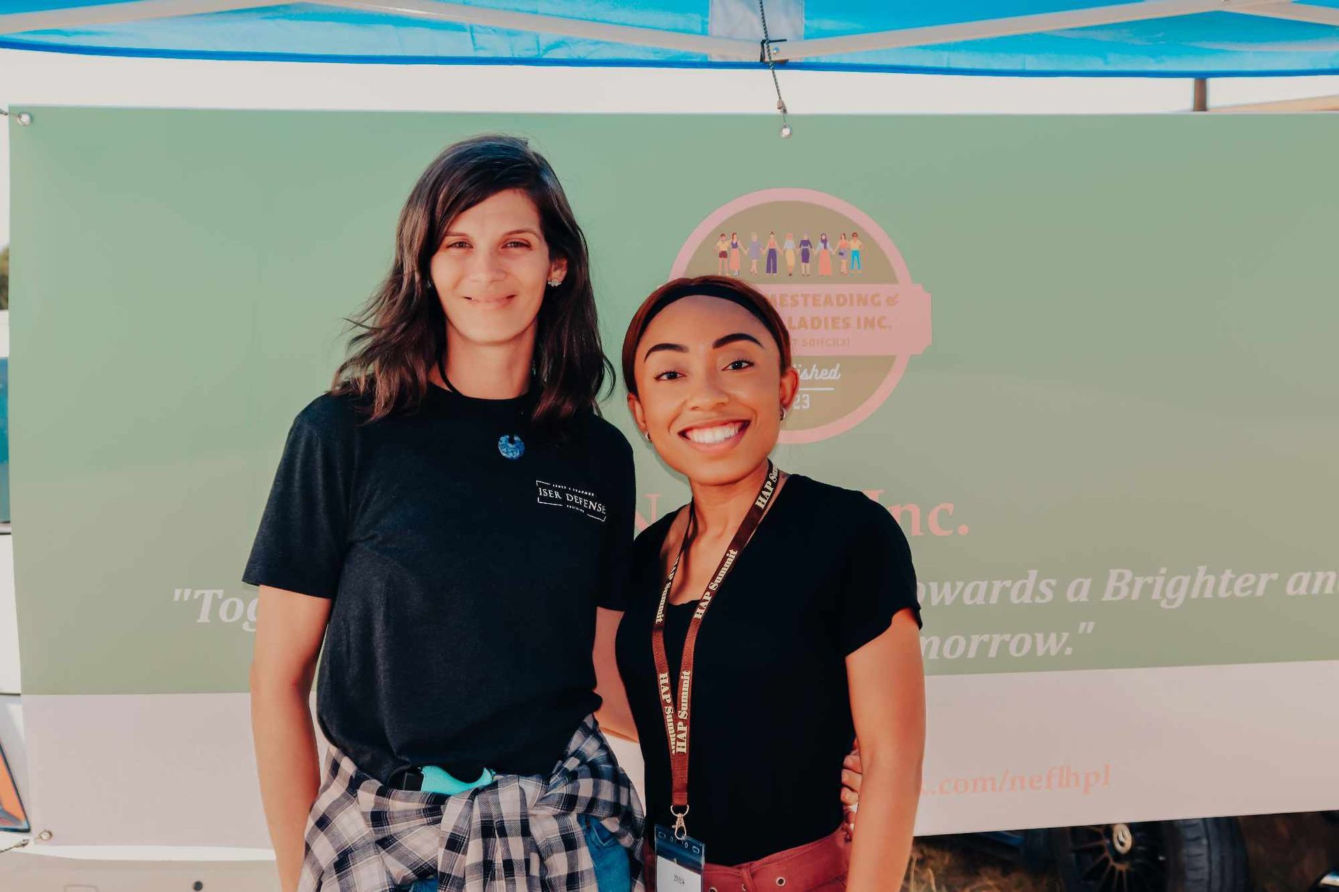 Two women are standing next to each other in front of a green sign.