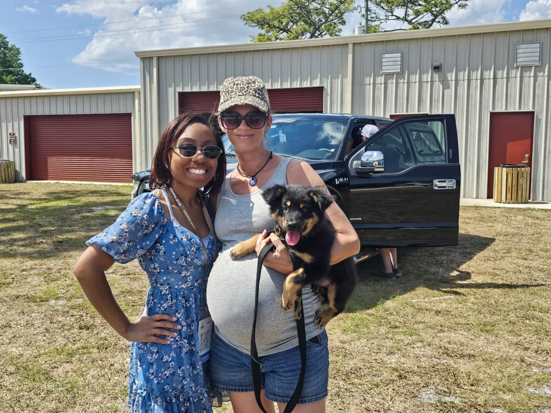 Two women are standing next to each other holding a dog in front of a truck.