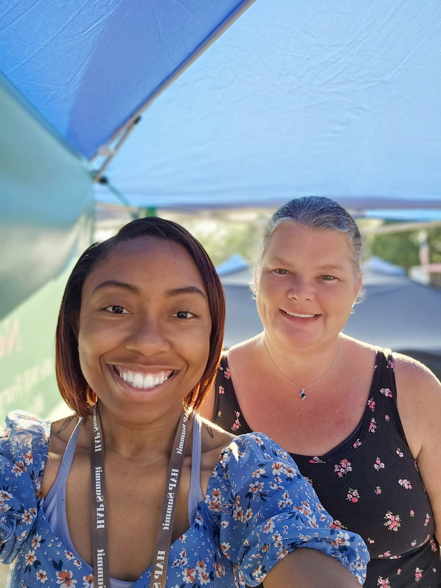 Two women are posing for a selfie under an umbrella.