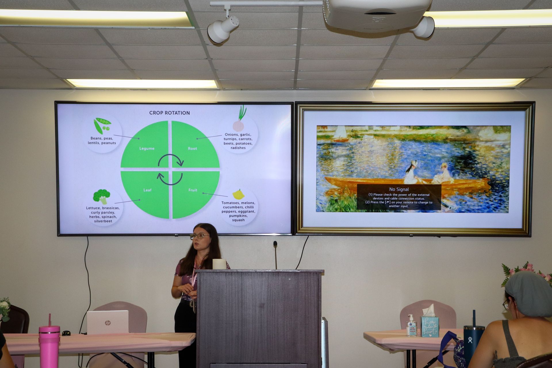 A woman is giving a presentation in front of a large screen in a classroom.