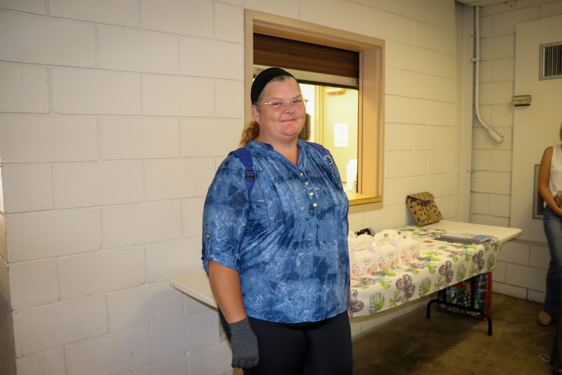 A woman in a blue shirt is standing in front of a table.