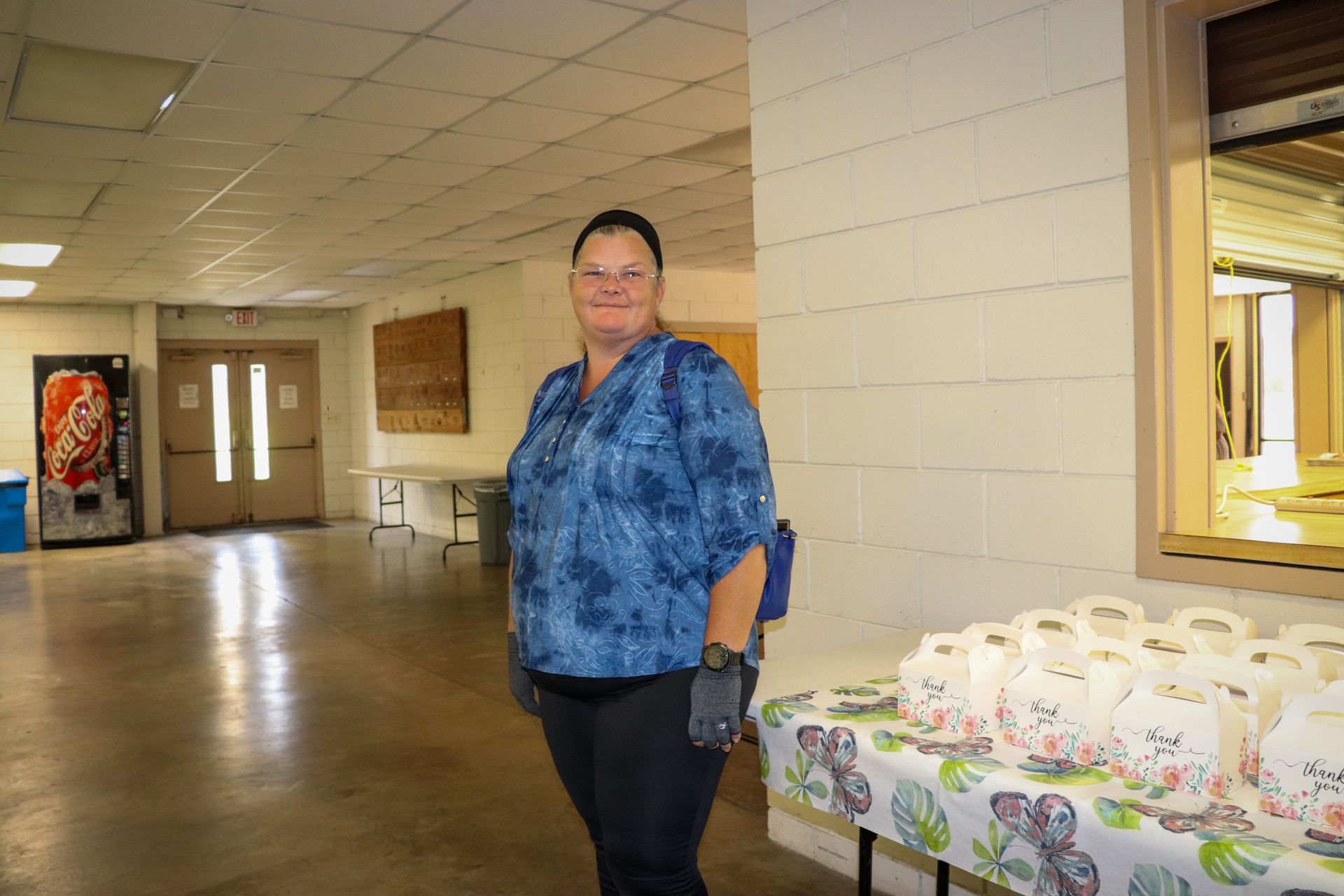 A woman in a blue shirt is standing in a hallway next to a table.