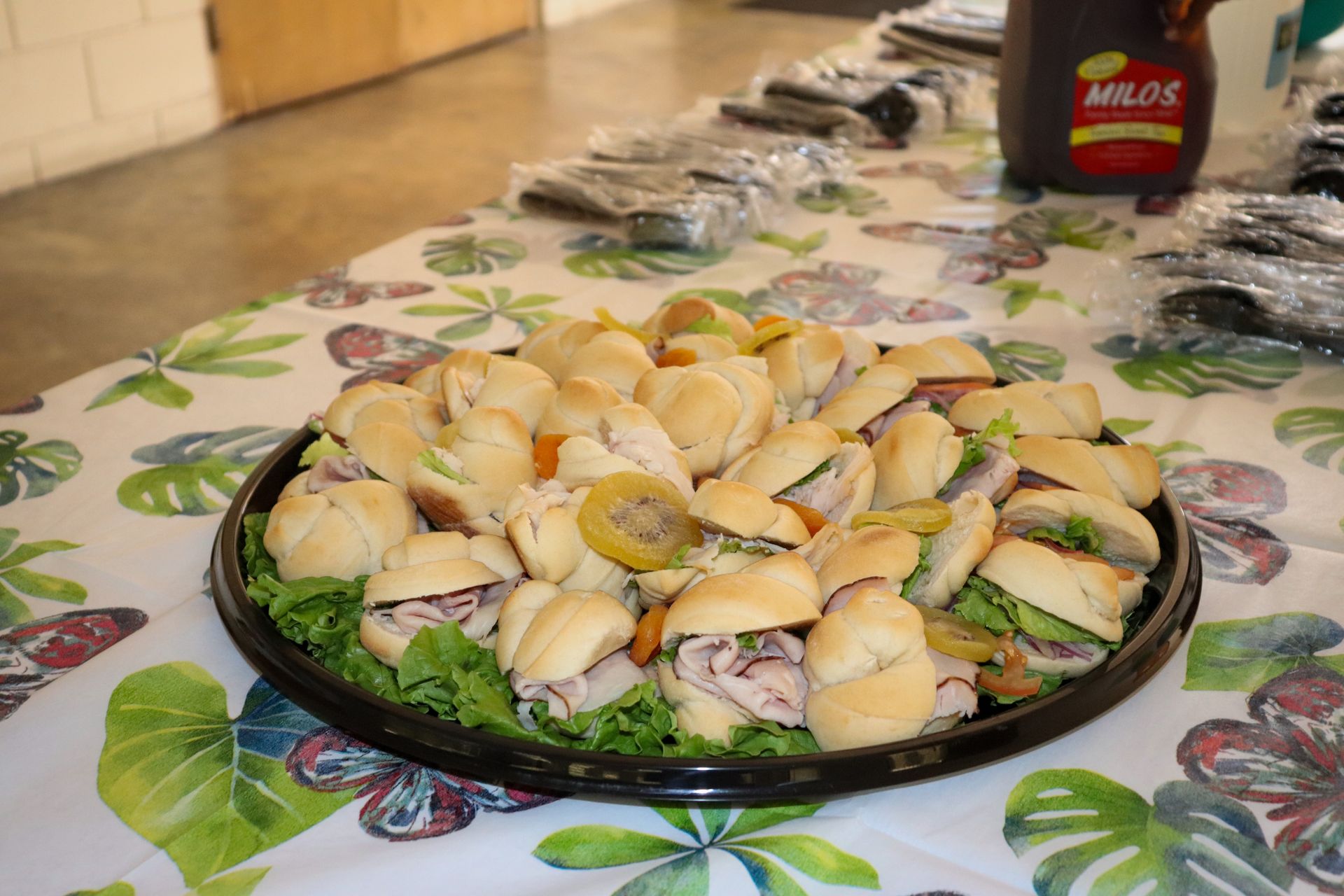 A tray of sandwiches on a table with a bottle of milo sauce in the background.