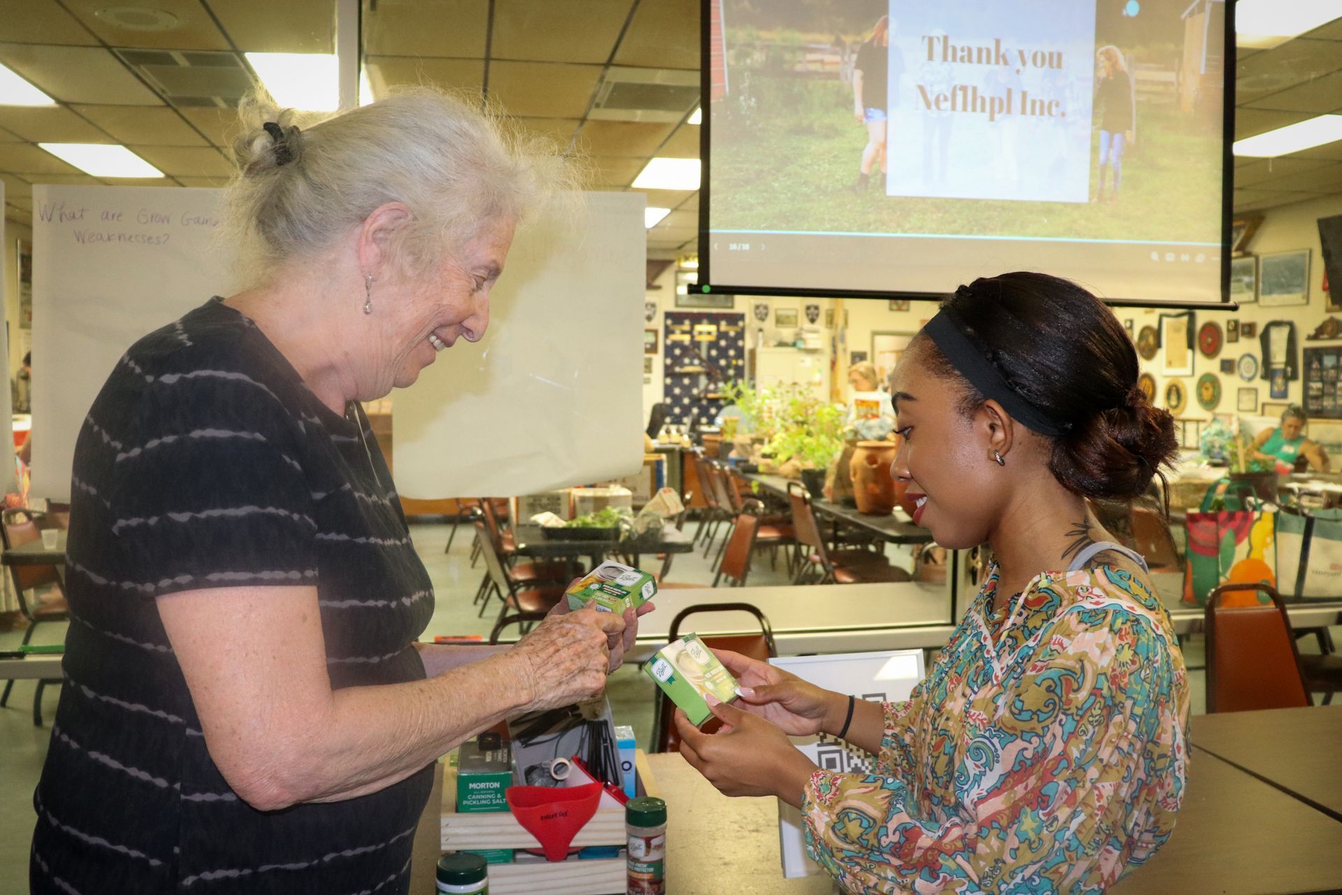 A woman is giving a gift to another woman in front of a projector screen.
