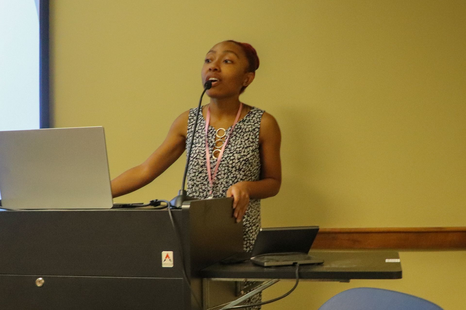 A woman stands at a podium with a laptop and a microphone