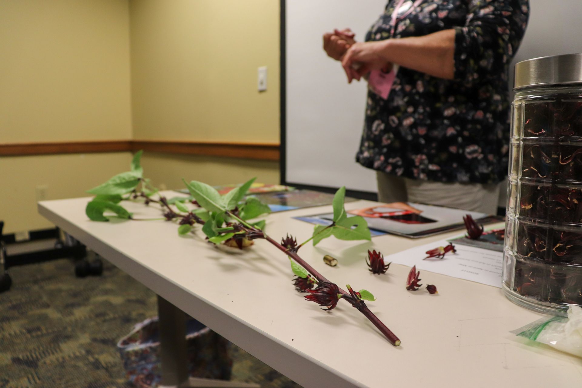 A woman is standing behind a table with flowers and leaves on it.