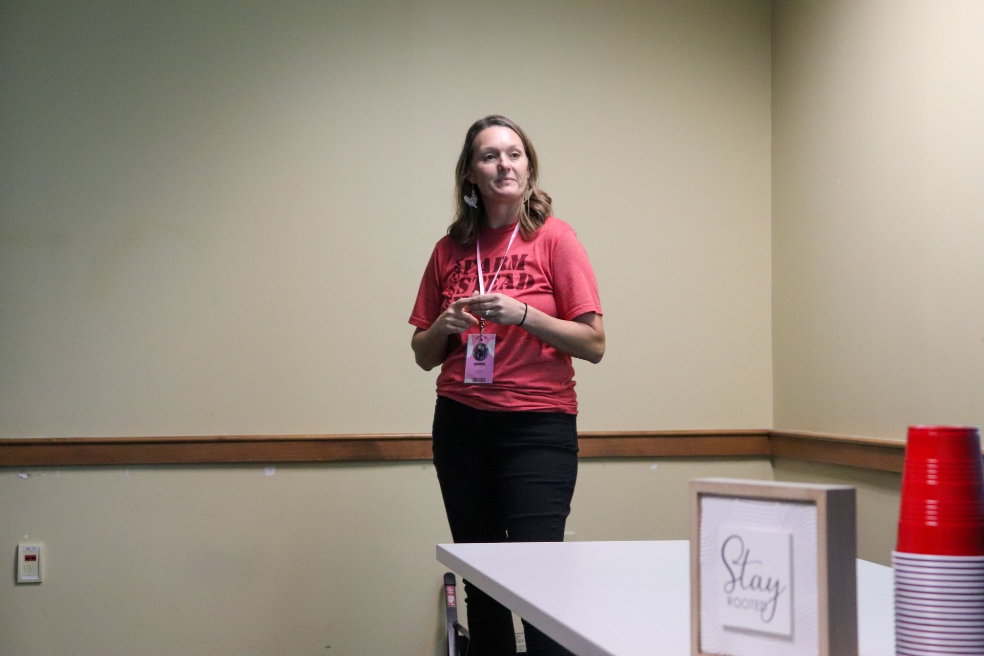 A woman in a red shirt is standing in a room next to a table.