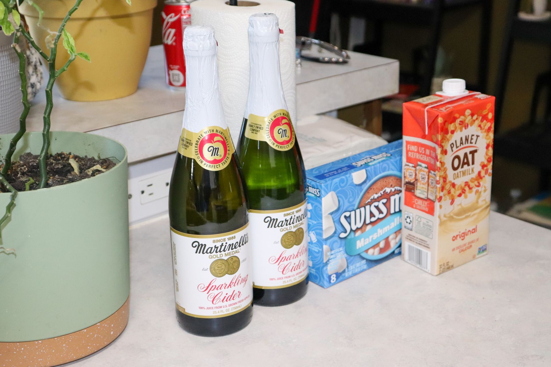 Two bottles of wine and a carton of oat milk are on a table.