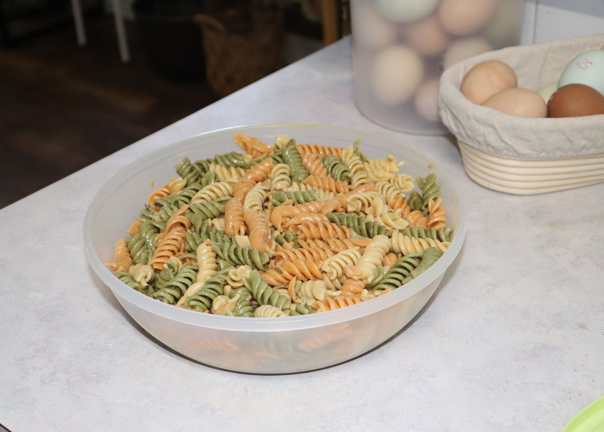 A bowl of pasta sits on a table next to a basket of eggs