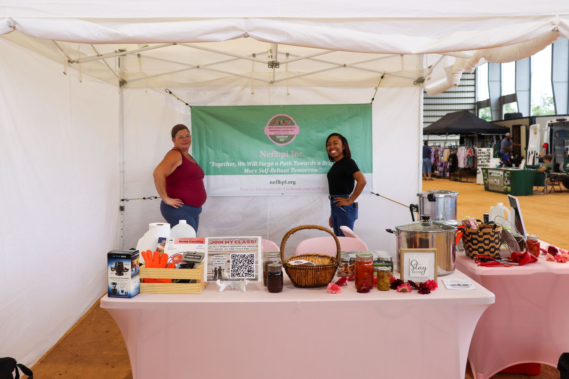 Two women are standing behind a table under a tent.